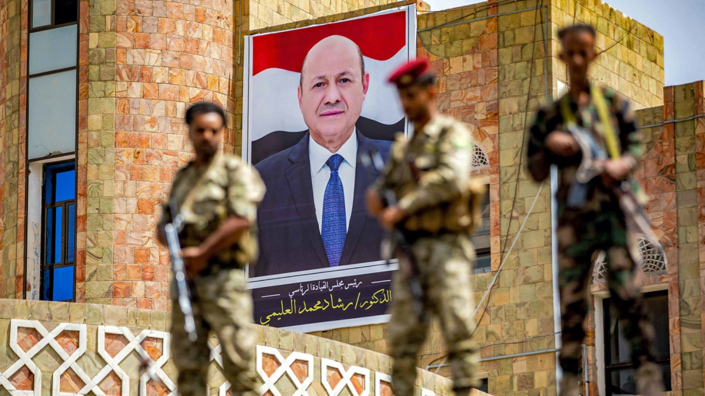 Soldiers loyal to the Aden-based Yemeni government stand guard before a poster showing the chairman of the presidential council Rashad al-Alimi on 25 May 2022 (AFP)