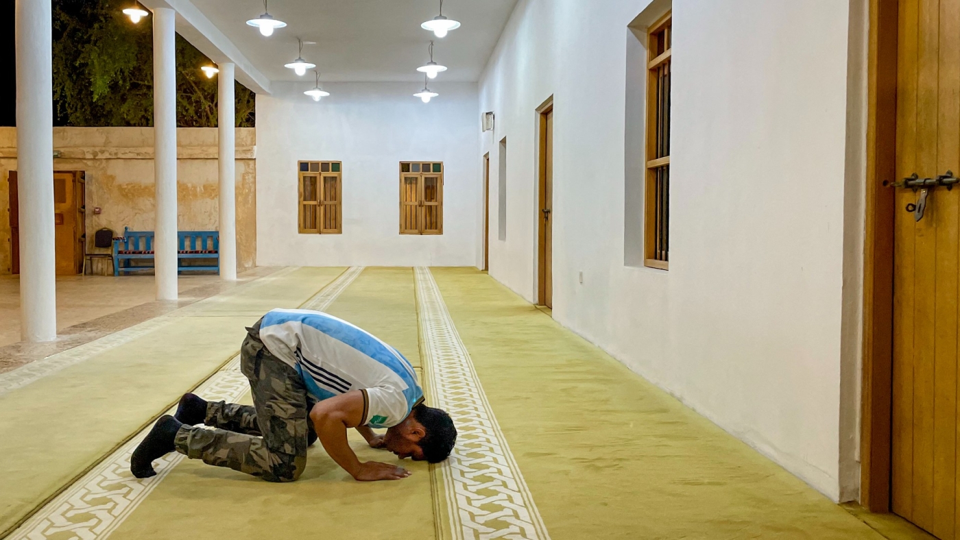 A man wearing an Argentina football shirt prays in a mosque in Al Wakrah, Qatar, on 4 December 2022 (AFP)