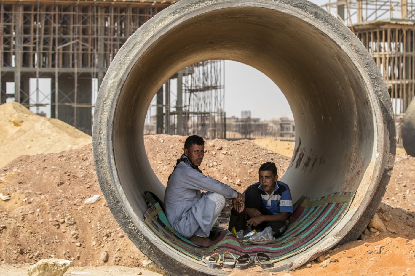 Labourers have a meal inside a concrete tube at a construction site at Egypt's New Administrative Capital megaproject, some 45 kilometres east of Cairo, on 3 August 2021 (AFP)