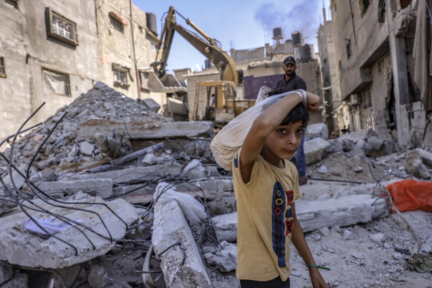 A Palestinian boy looks on as workers clear the rubble of a building destroyed by Israeli bombing during the 2021 war, in Rafah, Gaza, on 30 September 2021 (AFP)