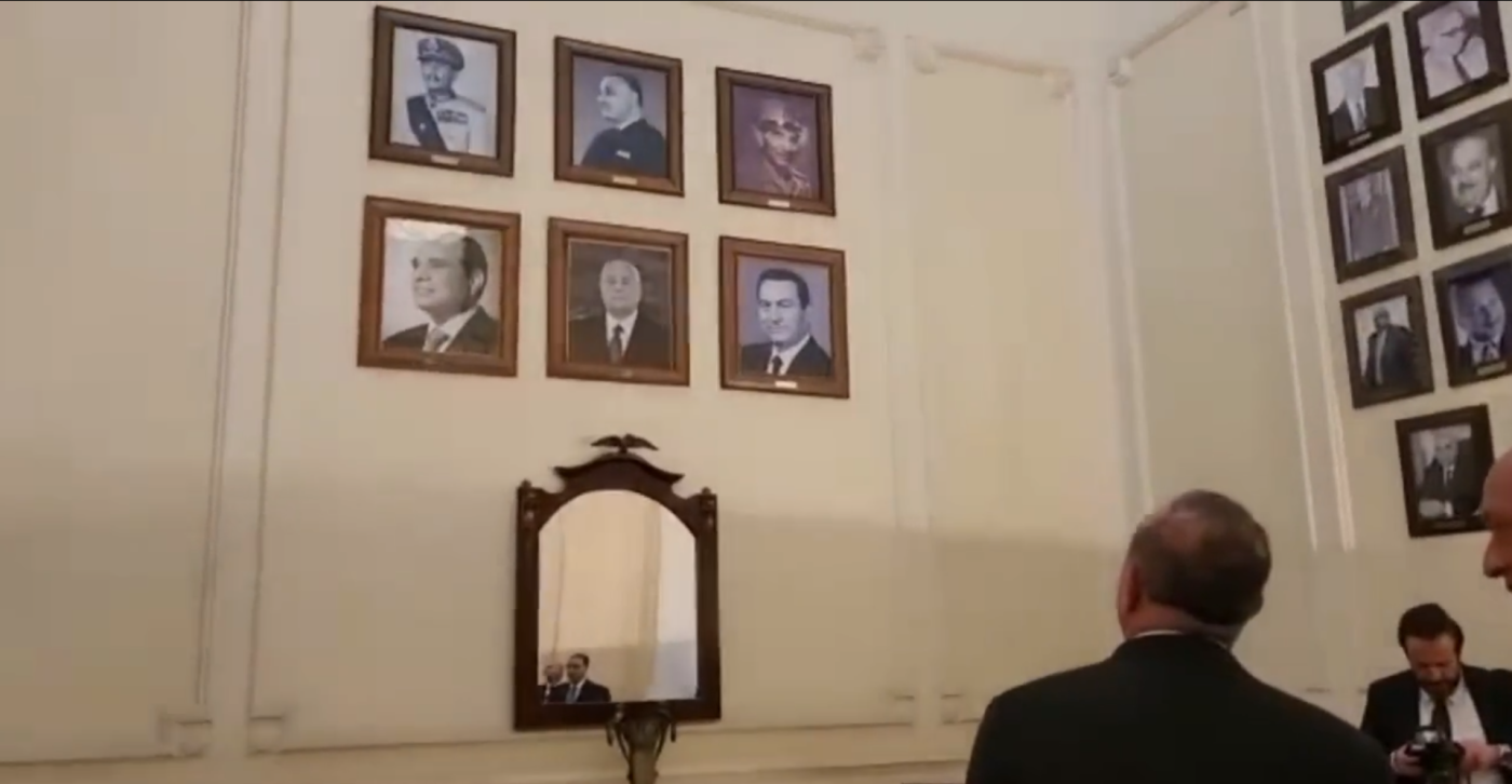 Turkey's Foreign Minister Mevlut Cavusoglu standing in front of a wall of pictures that features Egypt's presidents in Cairo (Screengrab)
