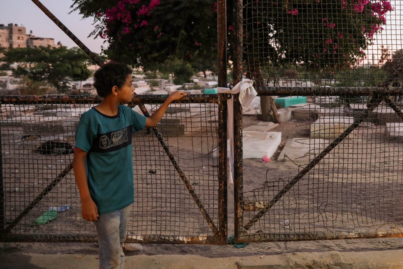 A Palestinian child looks through a fence at Falluja cemetery where five children, among them four cousins, were killed by an Israeli strike on 7 August 2022 in Gaza (MEE/Mohammed al-Hajjar)