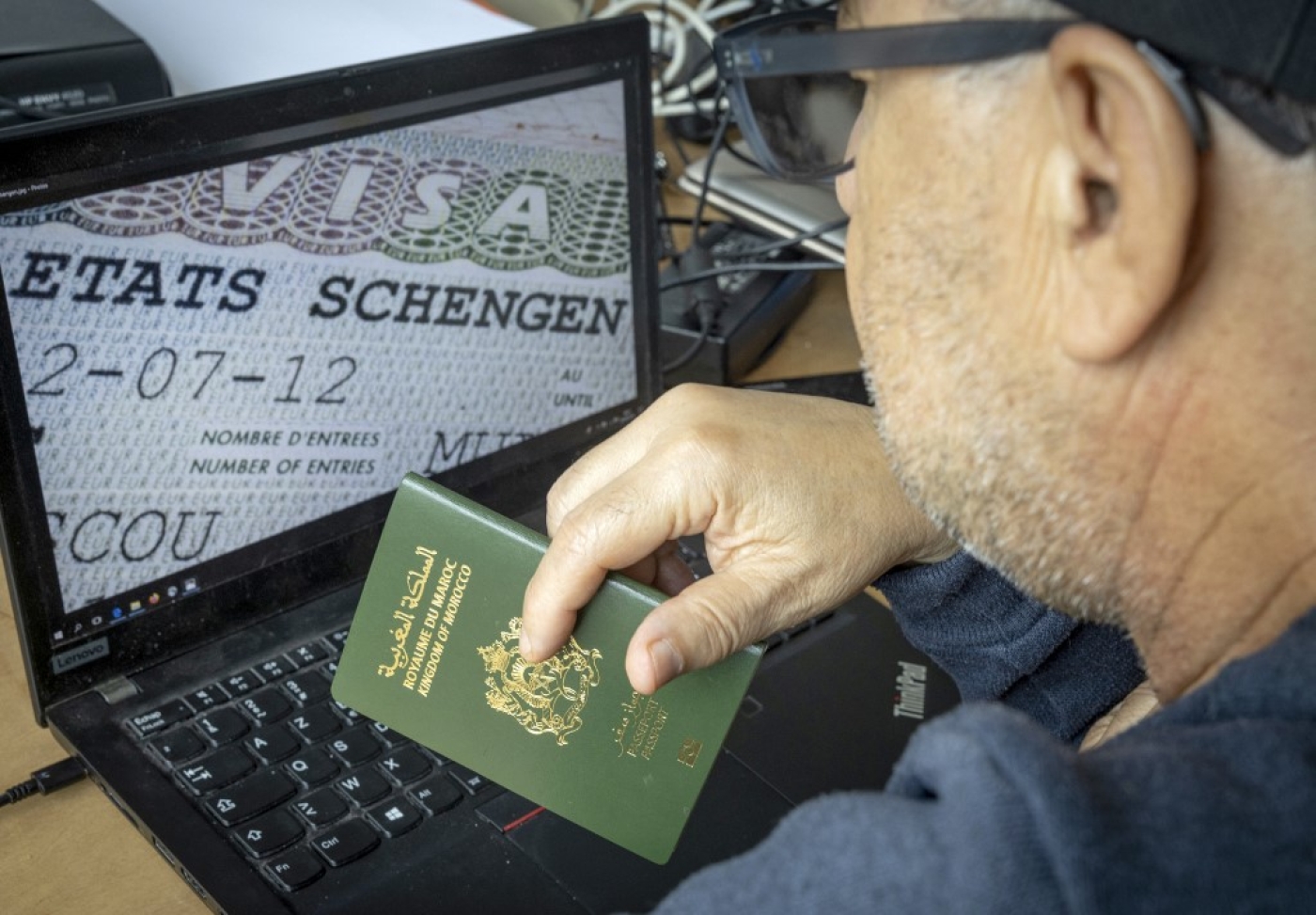 A Moroccan man holds his passport in front of his computer displaying a Schengen visa in the capital Rabat, on 28 September, 2021 (AFP)