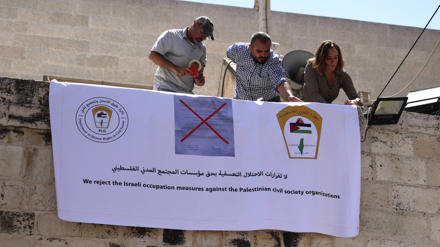 Activists hang a banner outside the Palestinian Al-Haq Foundation in the West Bank city of Ramallah after Israel raided and closed an entrance to their offices, on 18 August 2022.