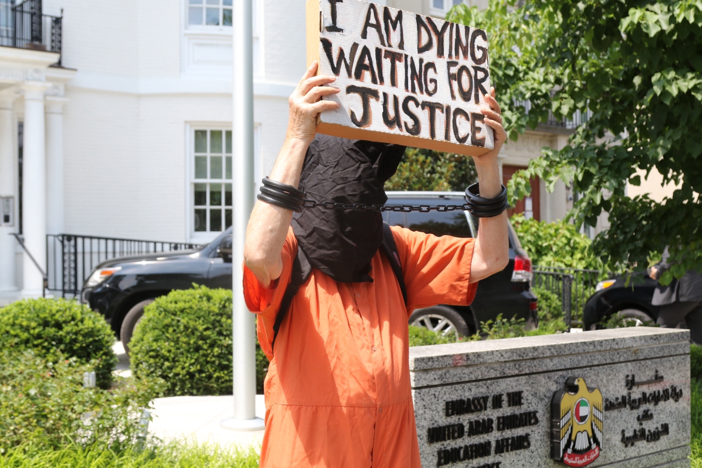 A protester wearing an orange jumpsuit with a black hood holds a sign in front of the UAE Cultural Attache in Washington on 22 July 2021.