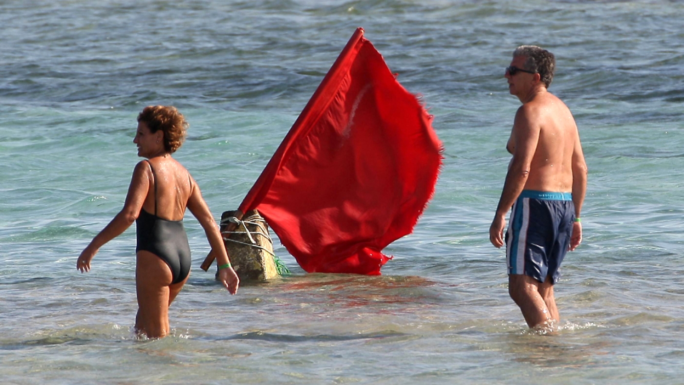Tourists walk past a red flag serving as a warning of shark sightings on a beach in the Red Sea resort of Sharm el-Sheikh on 8 December 2010 (AFP)