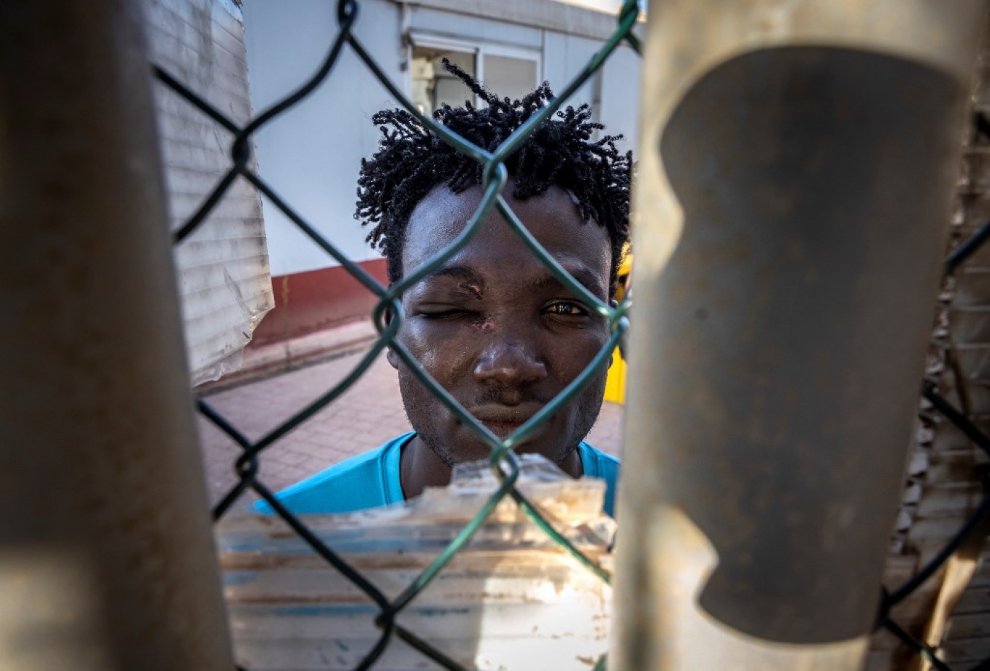 A Sudanese migrant looks through a fence in a temporary centre for migrants and asylum seekers on June 25, 2022 in Melilla (AFP)