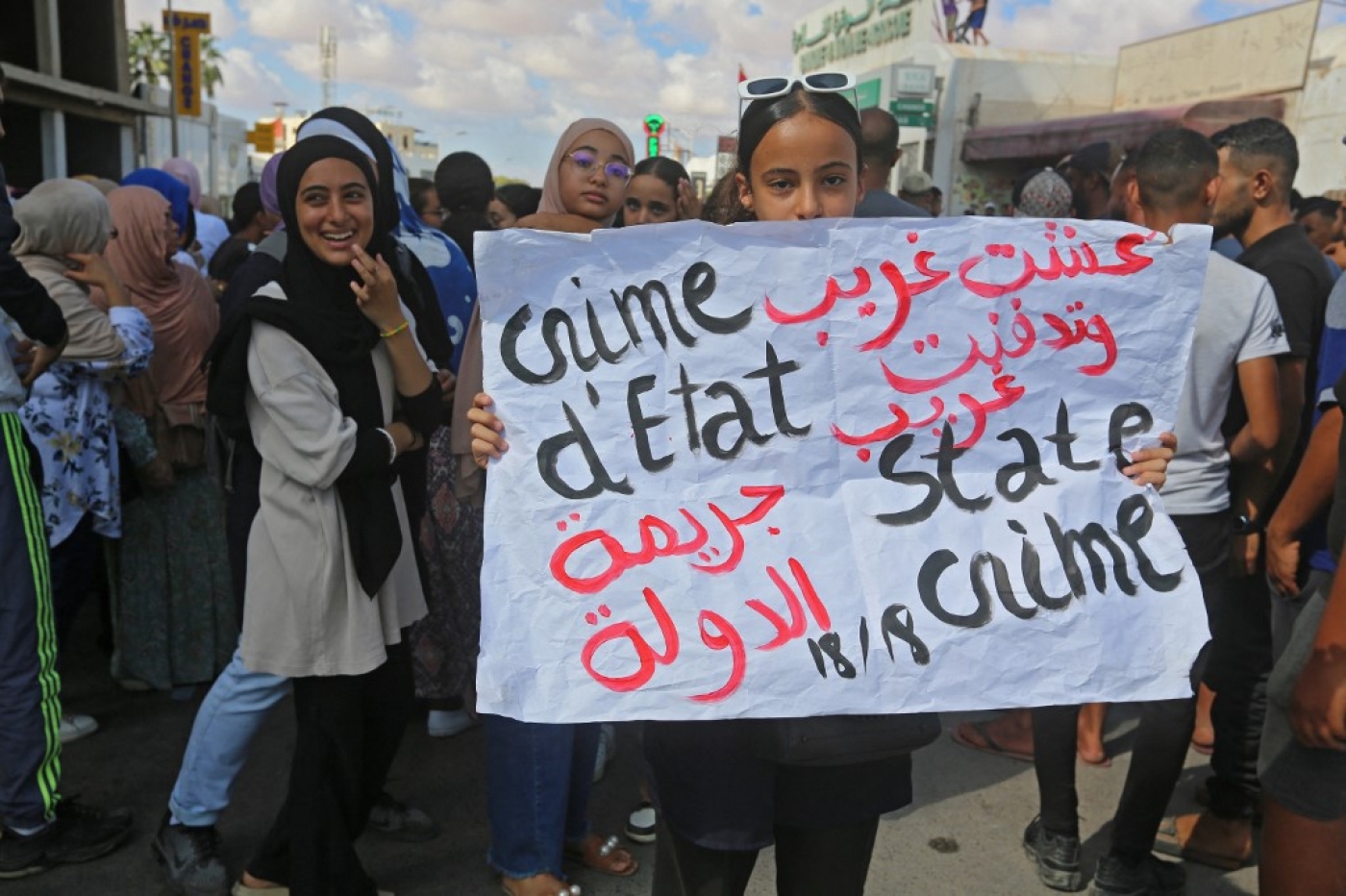 Une femme brandit une pancarte indiquant « J’ai vécu en étranger et j’ai été enterré en étranger » et « crime d’État », alors que les habitants de la ville côtière de Zarzis, dans le Sud-Est de la Tunisie, se rassemblent le 18 octobre lors d’une grève générale afin de réclamer une nouvelle recherche des proches portés disparus lors d’une tentative de migration clandestine en septembre (Fathi Nasri)