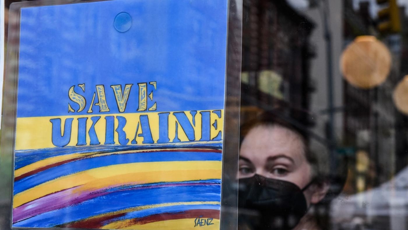 Une femme regarde par une fenêtre ornée d’affiches en soutien à l’Ukraine dans le quartier d’East Village à Manhattan (New York), le 24 avril 2022 (AFP)