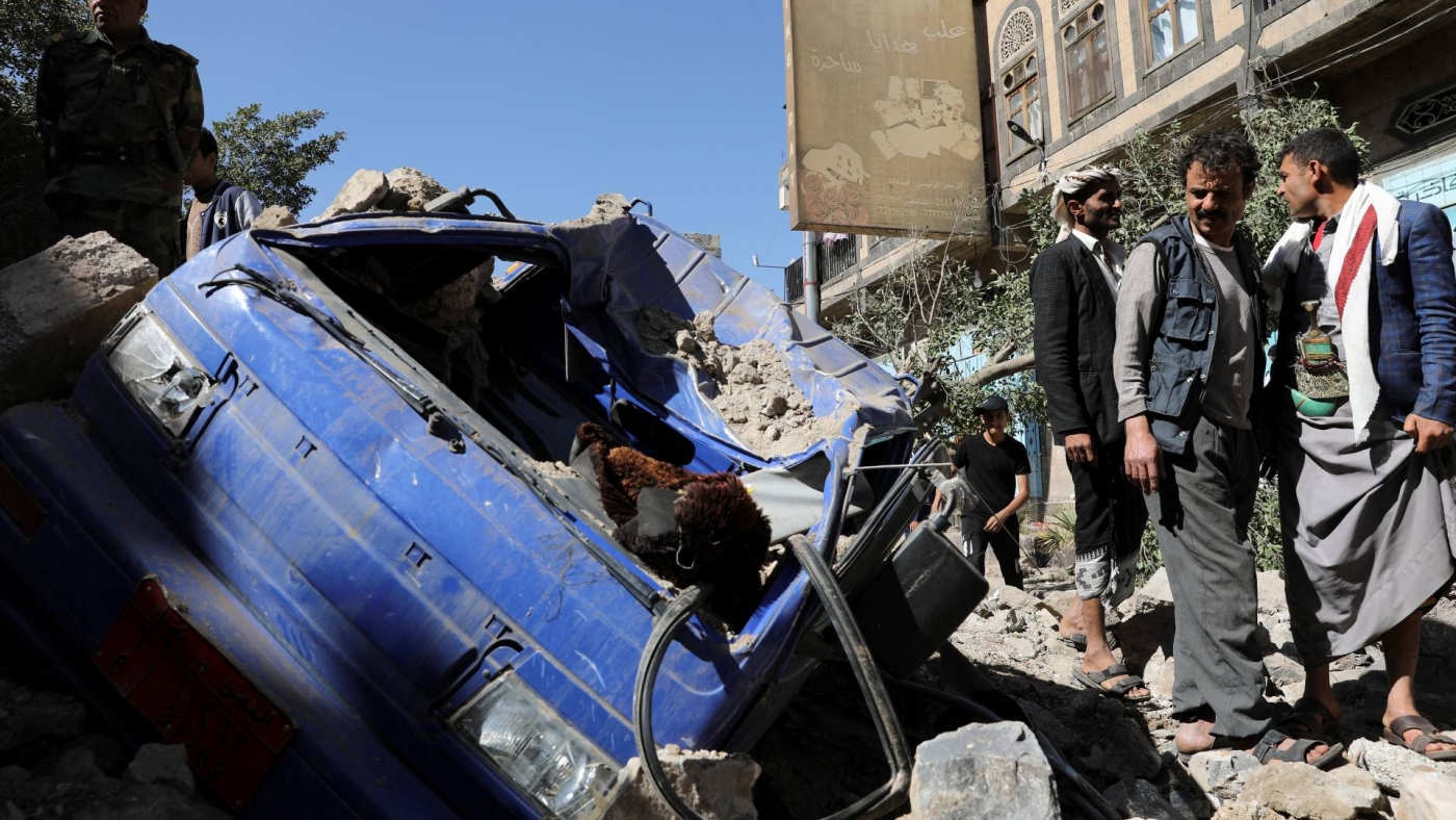 An officer and people stand by a vehicle destroyed by a Saudi-led air strike in Sanaa, Yemen on 24 December 2021.