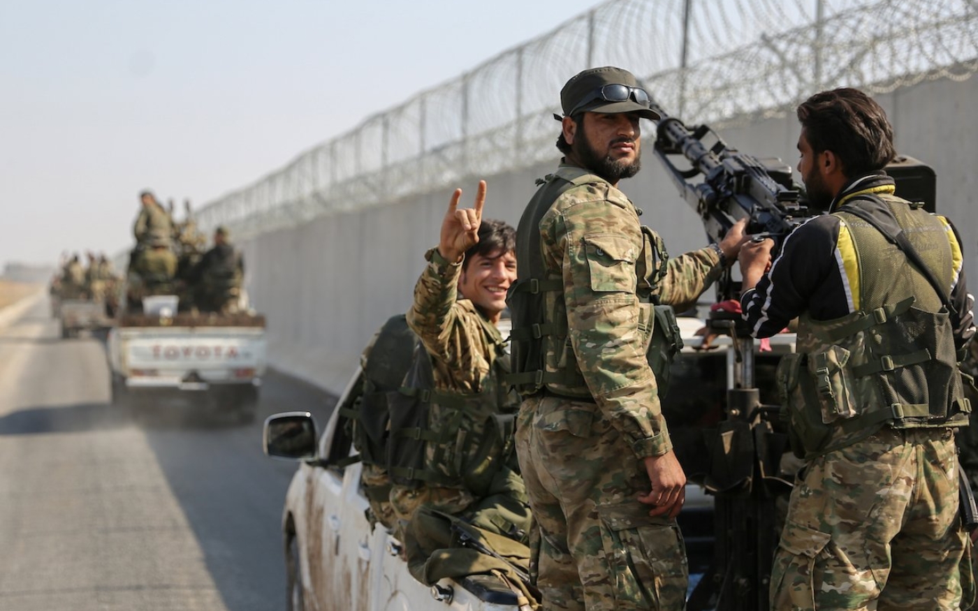 Un combattant syrien soutenu par la Turquie fait le geste des Loups gris tandis qu’un convoi passe la frontière syro-turque (AFP)