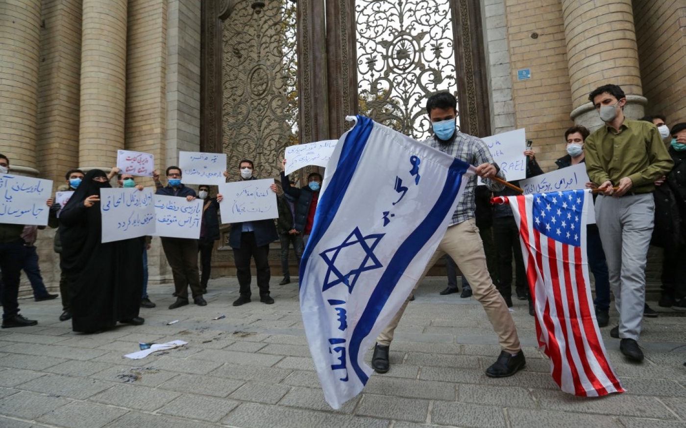 Des étudiants du groupe paramilitaire Basij s’apprêtent à brûler les drapeaux américain et israélien lors d’un rassemblement à Téhéran, le 28 novembre 2020 (AFP)