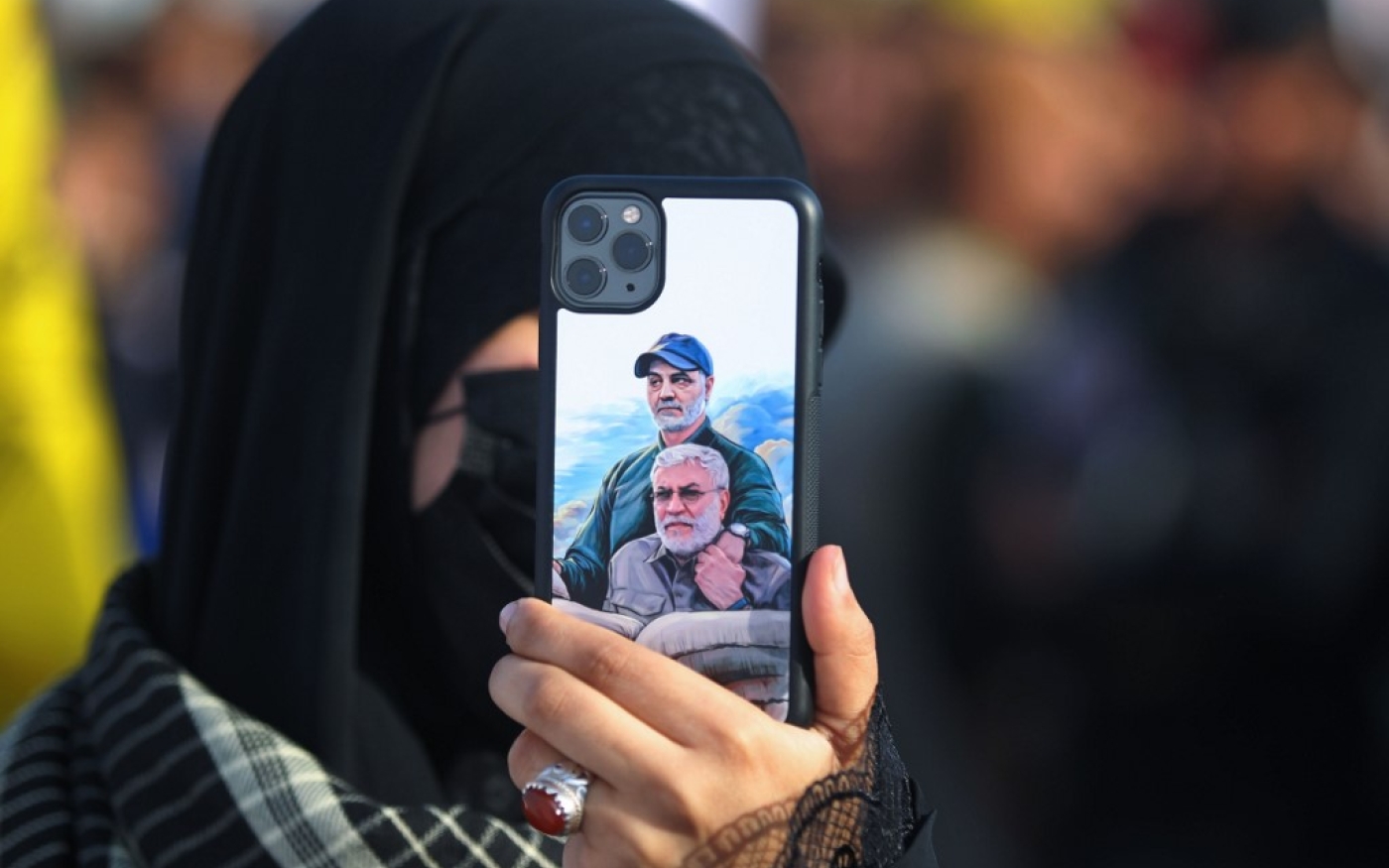 Un manifestant irakien montre un téléphone portable recouvert d’un portrait d’Abou Mahdi al-Mouhandis (en bas) et de Qasem Soleimani, lors d'un rassemblement à Bagdad, le 3 janvier 2021 (AFP)