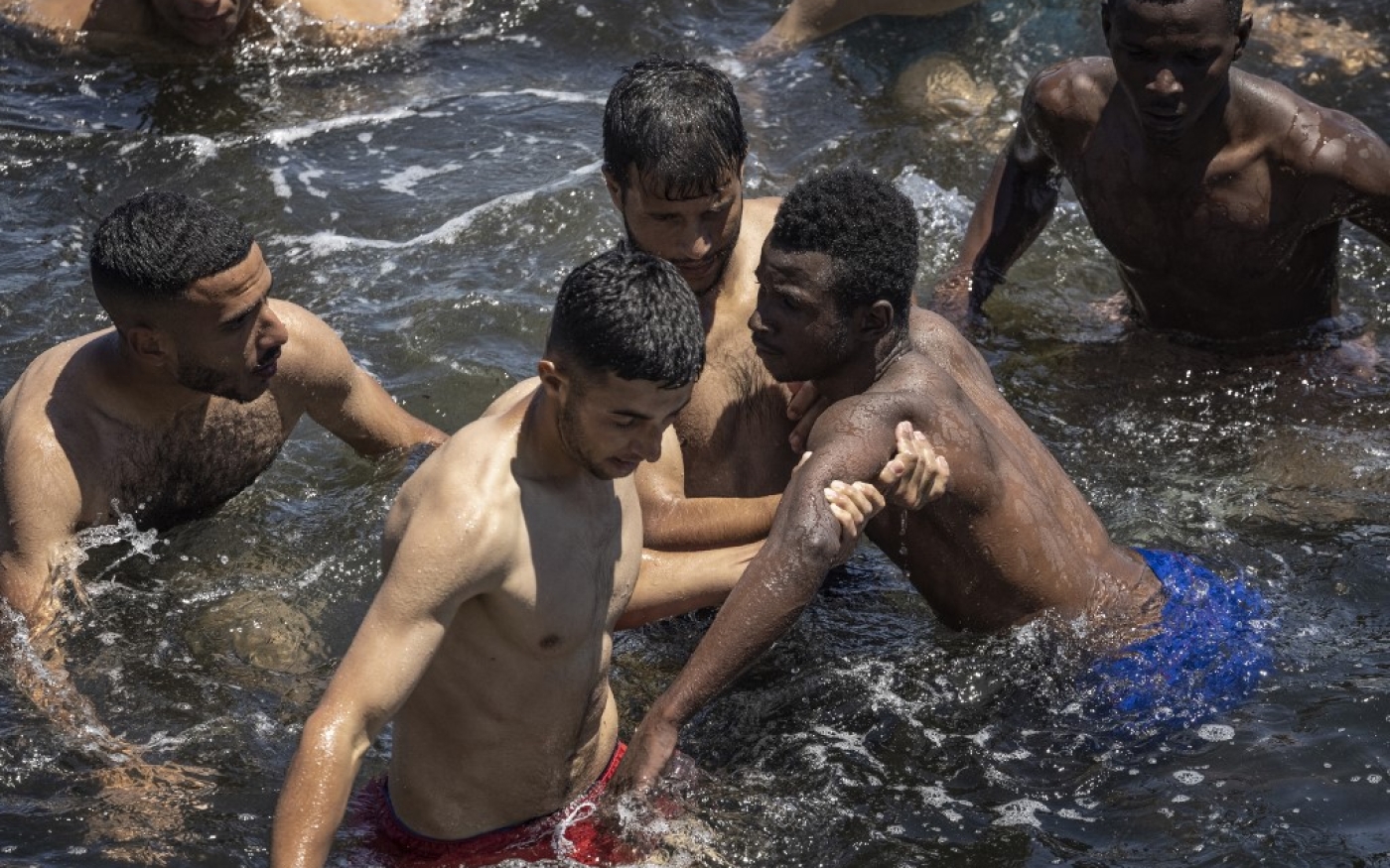 Des migrants marocains viennent en aide à un migrant subsaharien en difficulté dans l’eau, à la frontière entre le Maroc et Ceuta, le 19 mai 2021 (AFP/Fadel Senna)