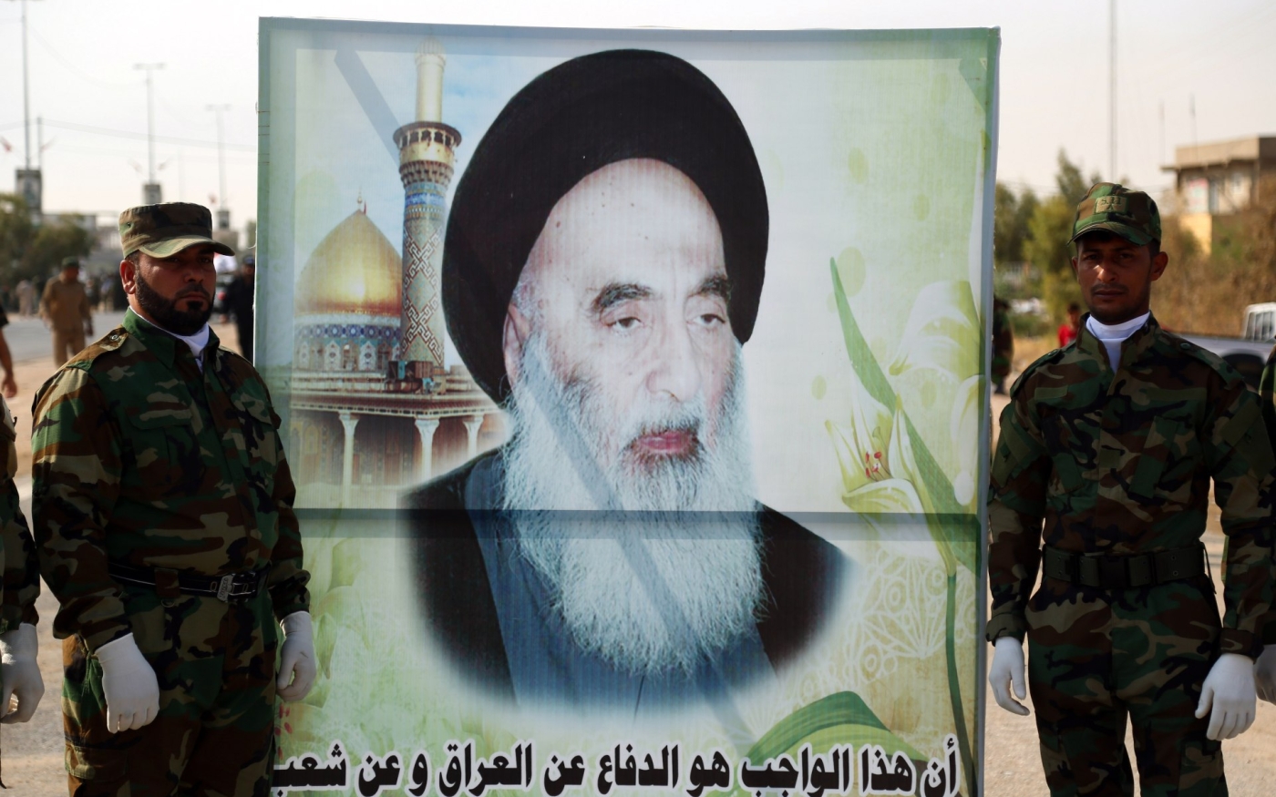 Des membres des Unités de mobilisation populaire portant une grande banderole représentant l’image du dignitaire chiite, l’ayatollah Ali al-Sistani, à Nadjaf (AFP)