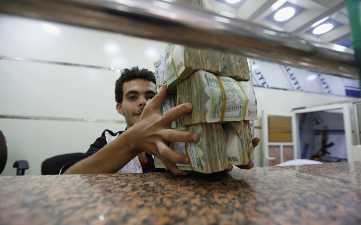 Un agent de change tient des liasses de monnaie yéménite dans un magasin de change à Sanaa (Reuters)