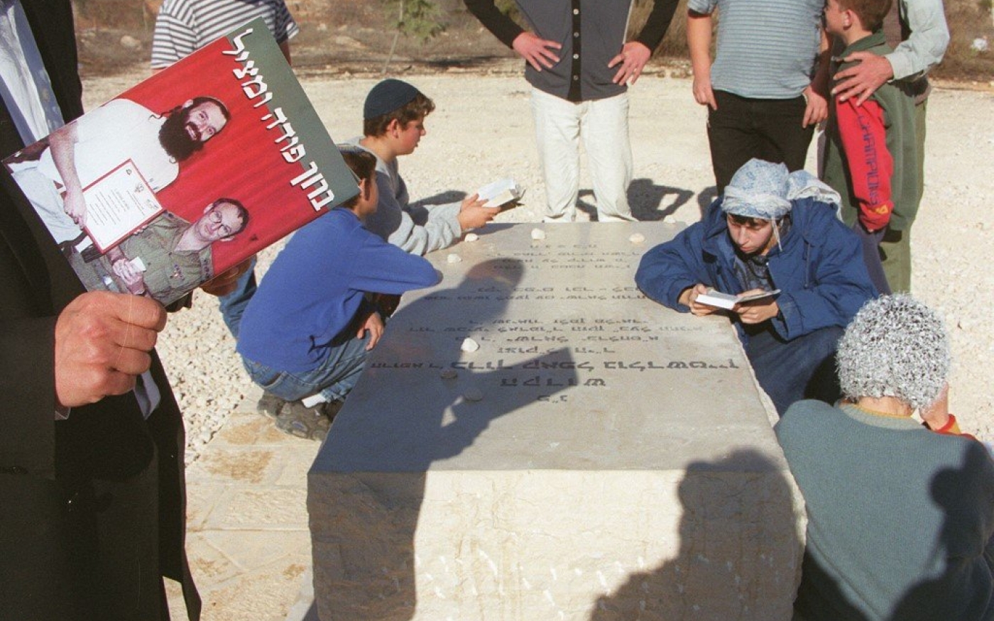 Un colon israélien lit un livre intitulé « Baruch le sauveur » sur la tombe de l’extrémiste Baruch Goldstein dans la colonie illégale de Kiriyat Arba, en Cisjordanie occupée, le 29 décembre 1999 (AFP)
