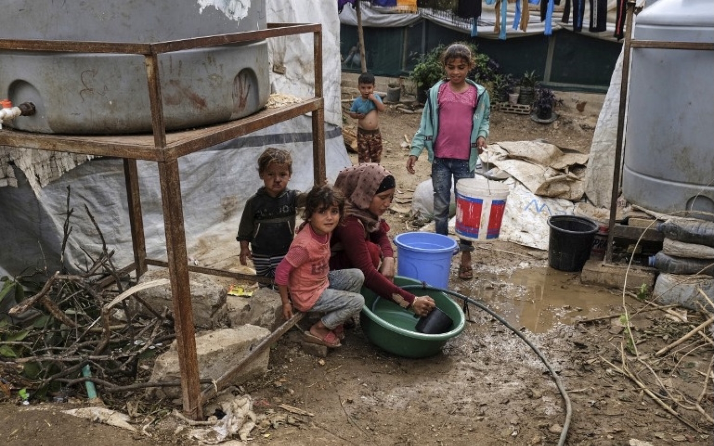 Des enfants autour d’une femme qui fait la vaisselle dans une bassine en plastique dans un camp de fortune pour les réfugiés syriens à Talhayat dans le Akkar, dans le Nord du Liban, le 26 octobre 2022 (AFP)