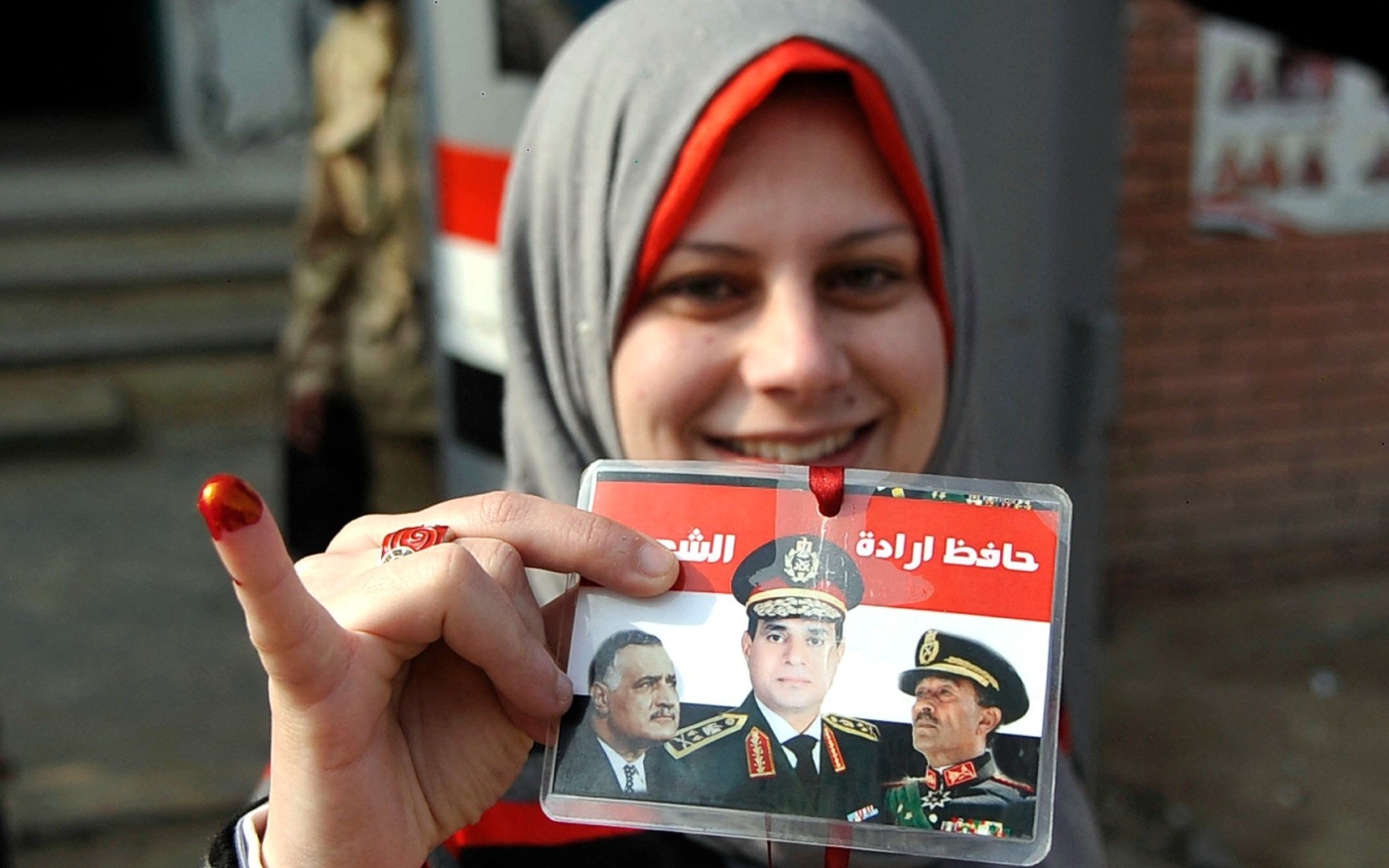 Une citoyenne égyptienne tient une carte sur laquelle figurent les portraits de Gamal Abdel Nasser et Anouar el-Sadate aux côtés d’Abdel Fattah al-Sissi, alors ministre de la Défense, le 15 janvier 2014 (AFP)
