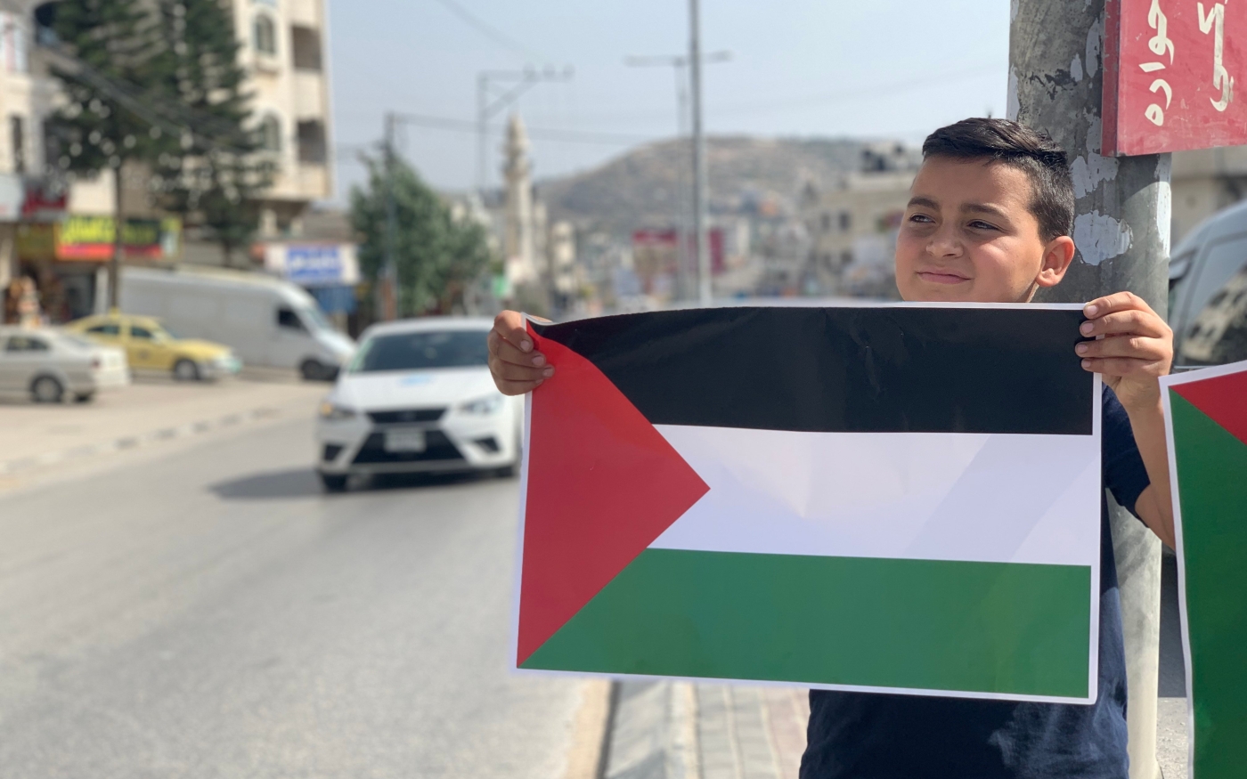Un enfant tient le drapeau palestinien à Huwara lors d’une campagne pour le hisser à travers la ville (MEE/ Shatha Hammad)