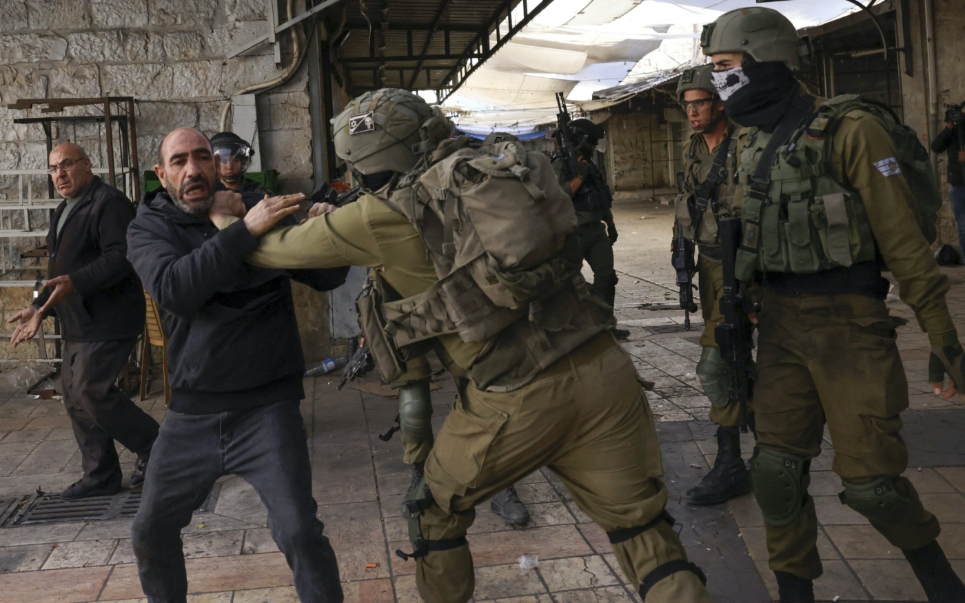 Les forces de sécurité israéliennes retiennent un Palestinien alors que des colons juifs défilent à Hébron (Cisjordanie occupée), le 19 novembre 2022 (AFP)