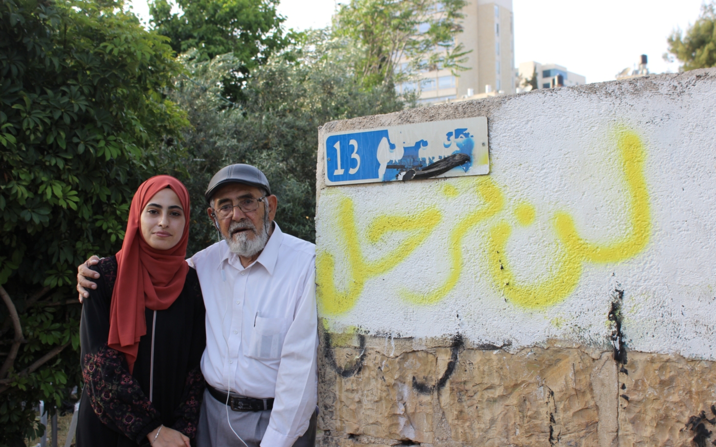 Muna et son père Nabil se tiennent contre un mur sur lequel « Nous ne partirons pas » est tagué en arabe (MEE/Aseel al-Jundi)