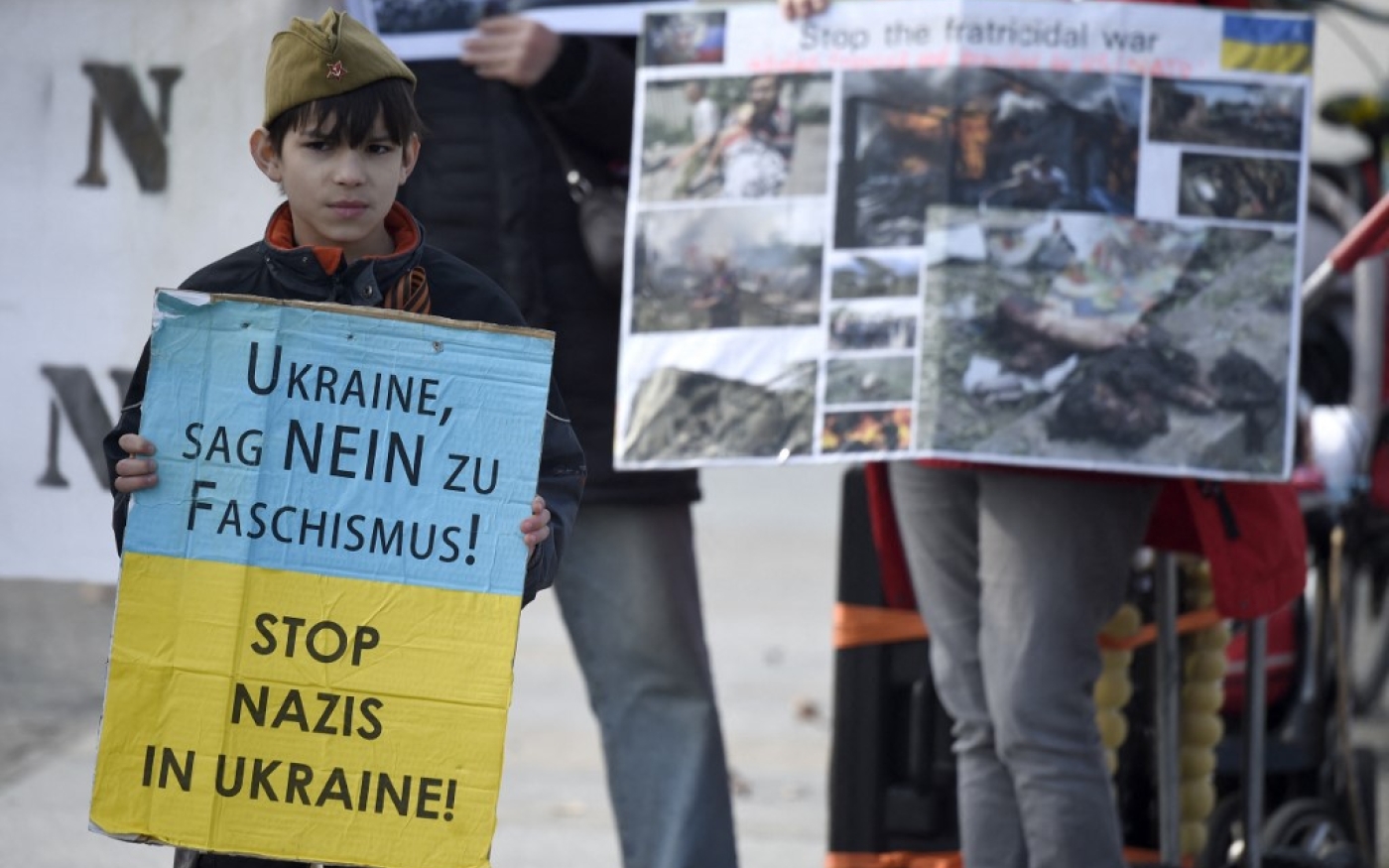 Des partisans des rebelles ukrainiens pro-russes brandissent des photos montrant des dégâts, tandis qu’un enfant tient une pancarte aux couleurs de l’Ukraine sur laquelle on peut lire « Ukraine, dis non au fascisme » et « Stop aux nazis en Ukraine ! », le 16 mars 2015 à Berlin (AFP)