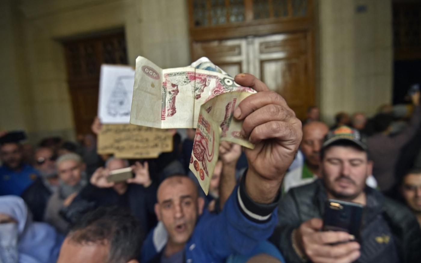 Un Algérien agite des billets de banque à l’entrée du tribunal de Sidi M’Hamed, à Alger, le 2 décembre 2019, avant l’ouverture d’un procès pour corruption d’anciennes personnalités politiques et économiques (AFP/Ryad Kramdi)