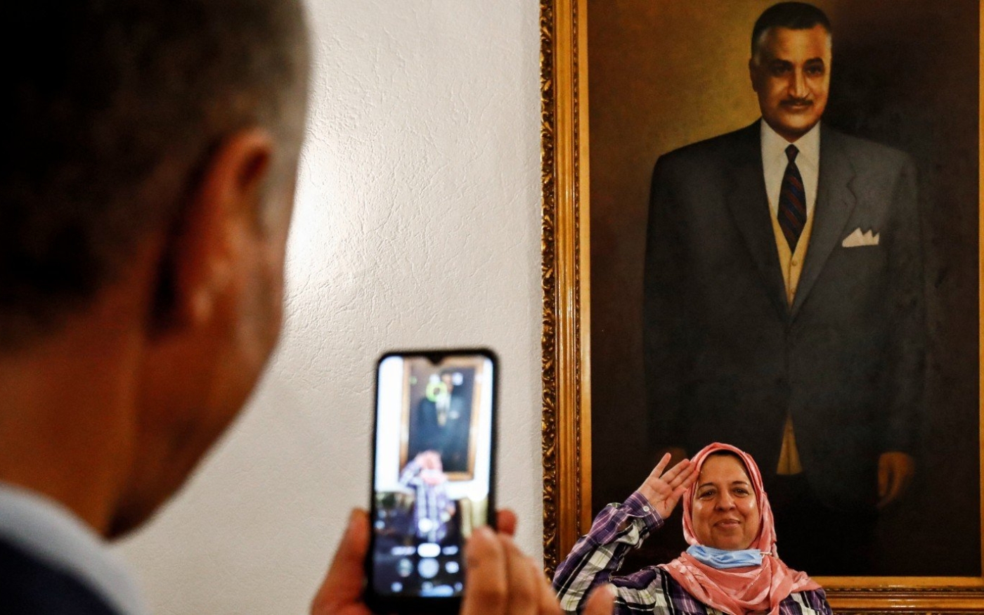 Un homme photographie avec son téléphone une femme effectuant un salut devant un tableau représentant le président égyptien Gamal Abdel Nasser à son mausolée au Caire, le 28 septembre 2020 (AFP)