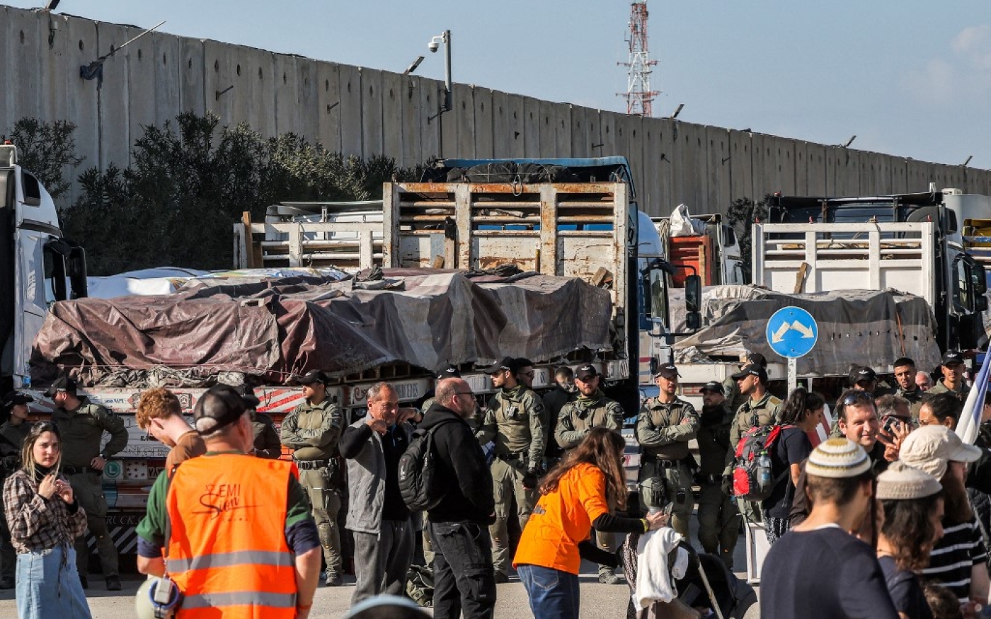 Les forces de sécurité israéliennes se tiennent près des camions égyptiens apportant de l’aide humanitaire dans la bande de Gaza, du côté israélien du poste frontière de Kerem Shalom, le 6 février 2024, alors que des manifestants israéliens de droite se rassemblent pour empêcher les camions d’entrer (AFP/Ménahem Kahana)