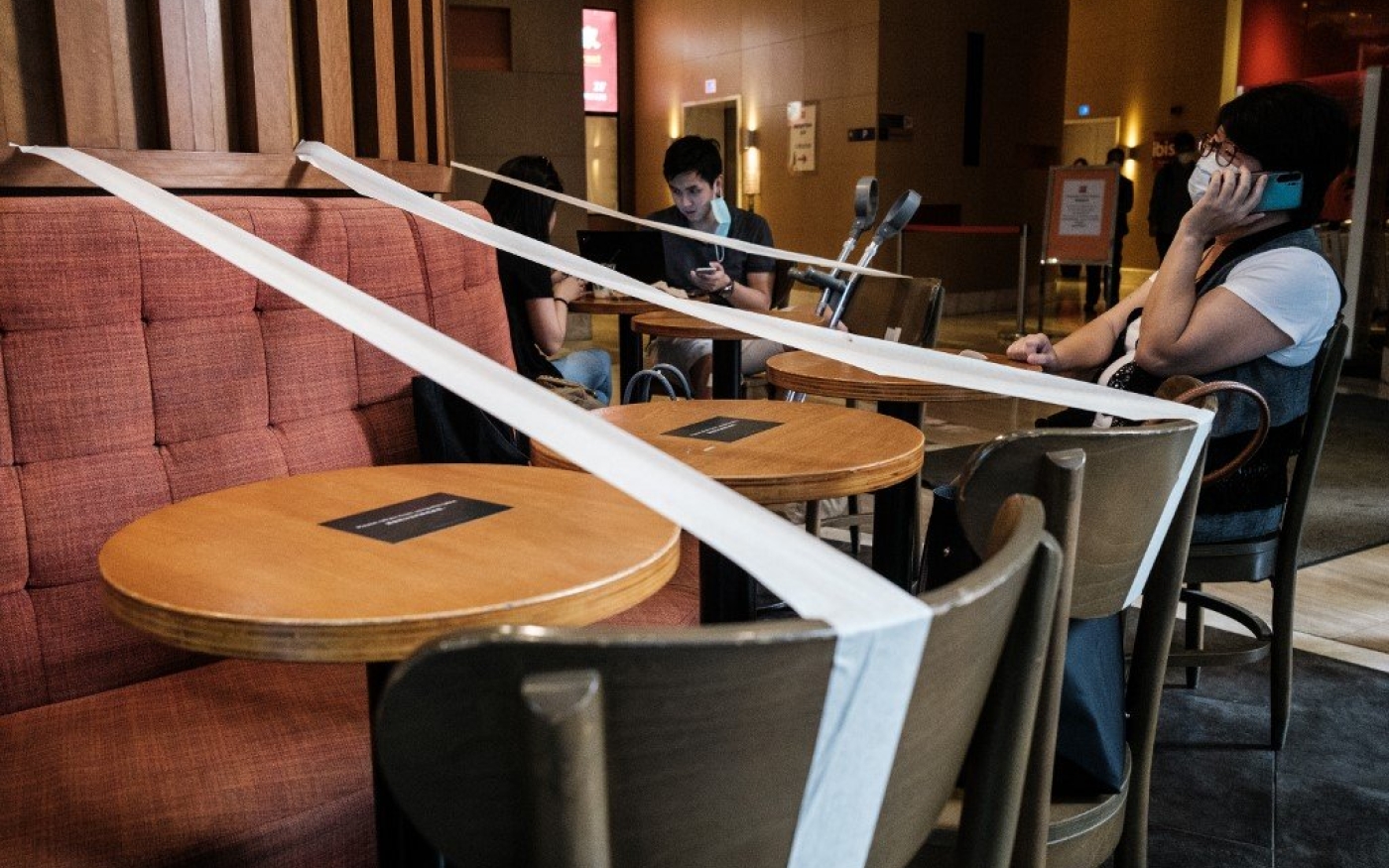 Des clients sont assis dans un café où du ruban adhésif barre toutes les autres tables pour imposer la distanciation physique à Hong Kong, le 21 avril (AFP)