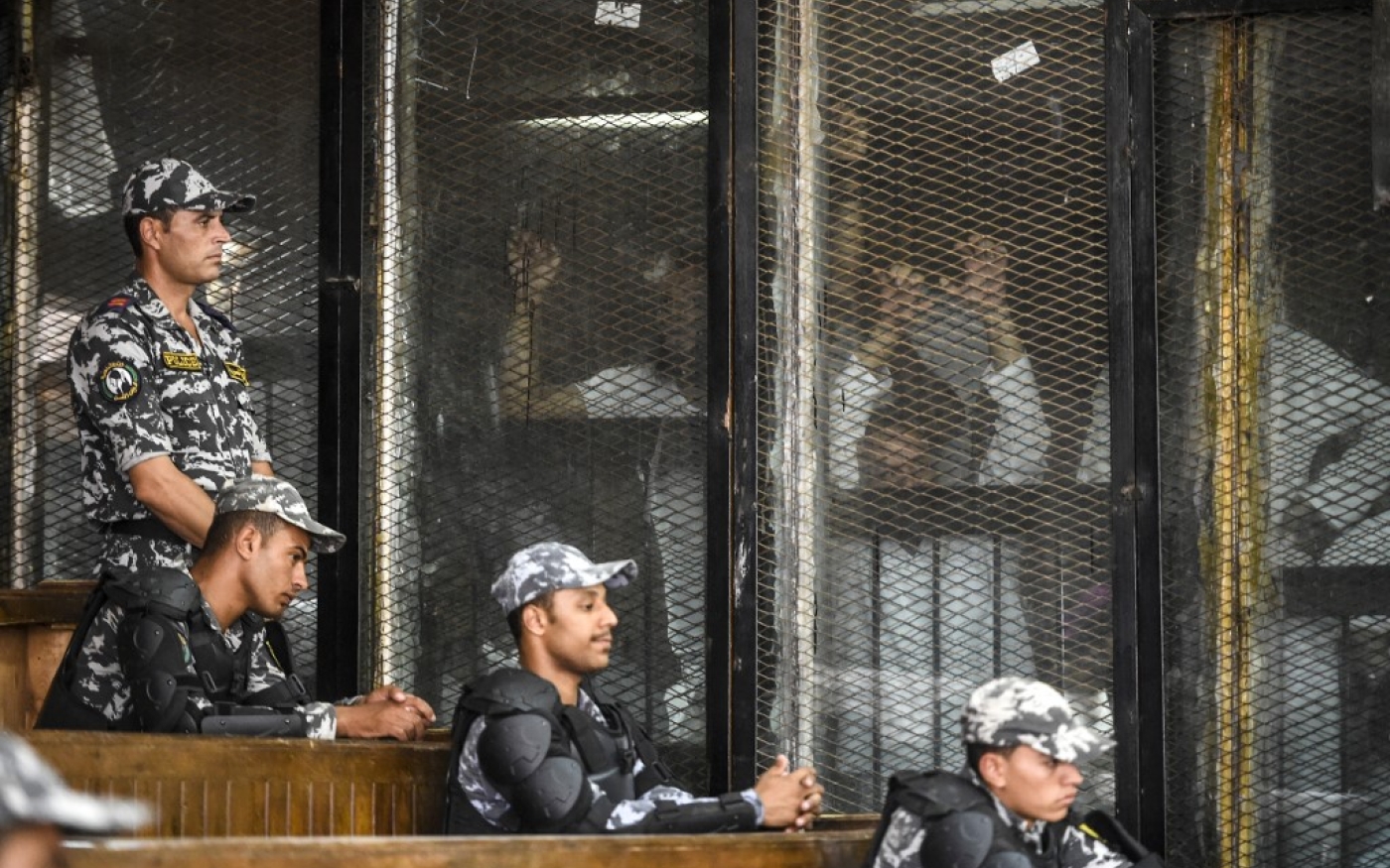 Des membres des Frères musulmans d’Égypte sont aperçus derrière des grillages et des vitres lors de leur procès en 2018 au Caire (AFP)