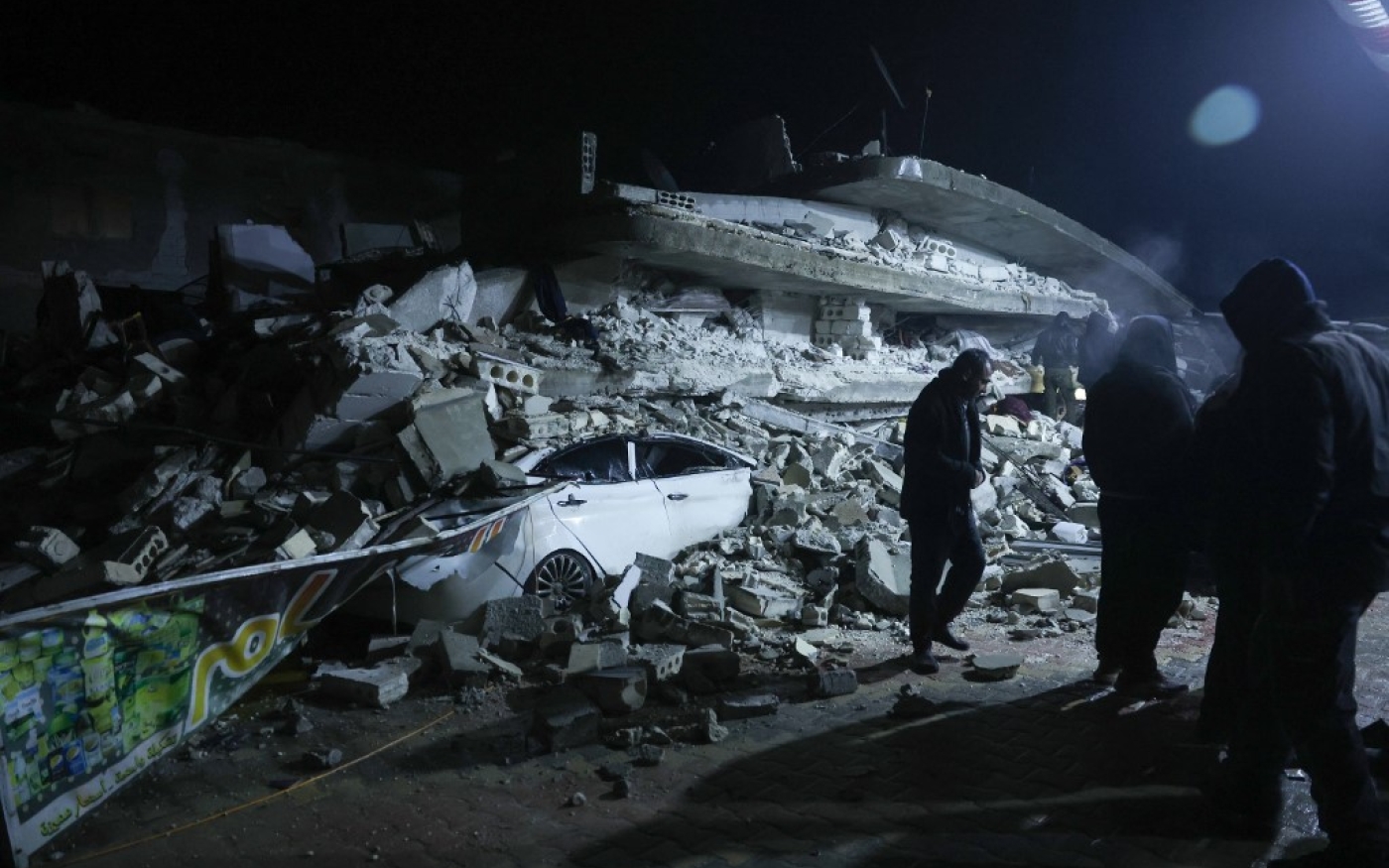 Des habitants sont rassemblés devant les décombres d’un immeuble qui s’est effondré à Azmari, au nord d’Idleb en Syrie, près de la frontière avec la Turquie (AFP/Omar Haj Kadour)