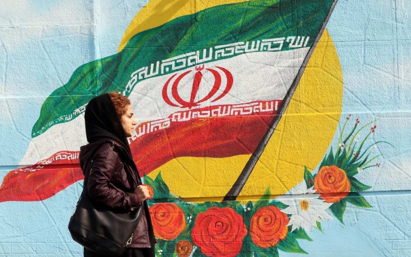 Une Iranienne passe devant une fresque représentant le drapeau national, à Téhéran (AFP)