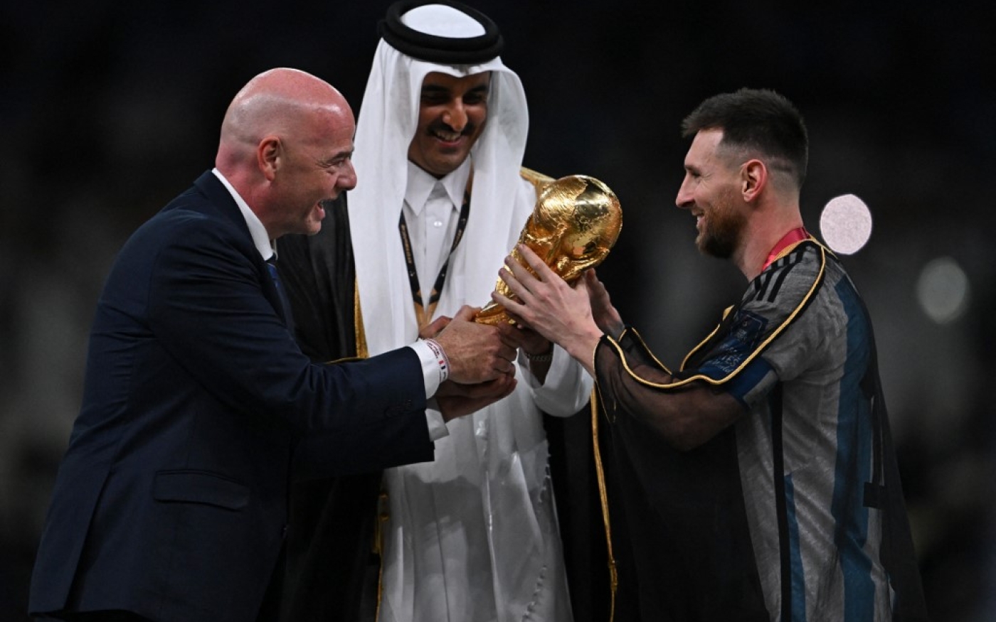 Le président de la FIFA, Gianni Infantino, et l’émir du Qatar, Tamim ben Hamad al-Thani, remettent le trophée de la Coupe du monde à Lionel Messi, à Doha, le 18 décembre 2022 (AFP/Paul Ellis)