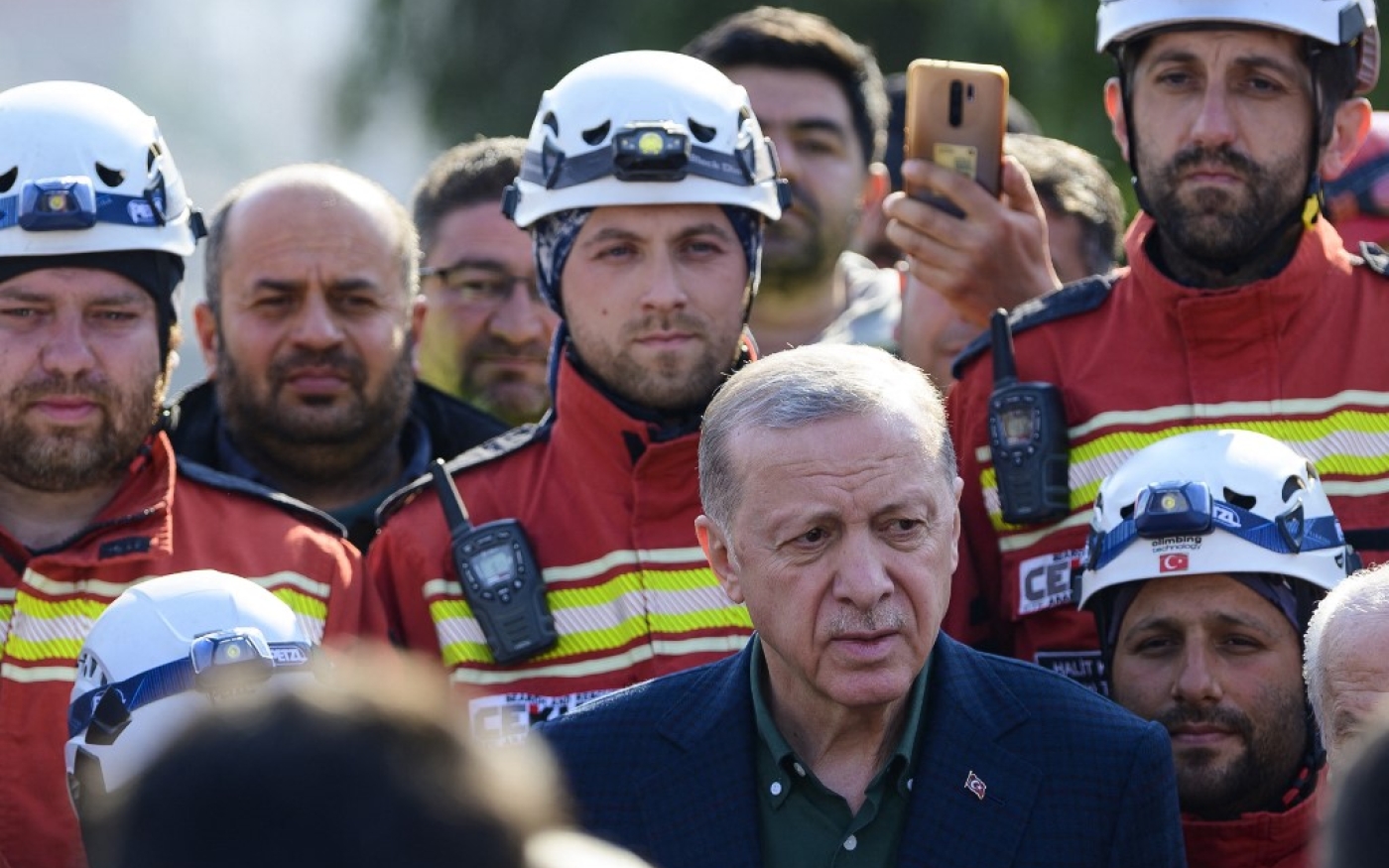 Le président turc Recep Tayyip Erdoğan  se tient aux côtés des secouristes lors de sa visite dans la province du sud-est de Hatay, durement touchée par deux tremblements de terre, le 20 février 2023 (AFP/Yasin Akgul)