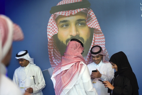 Saudis check their phones in front of a poster of Saudi Crown Prince Mohammed bin Salman in Riyadh on 15 November 2017 (Fayez Nureldine/AFP)