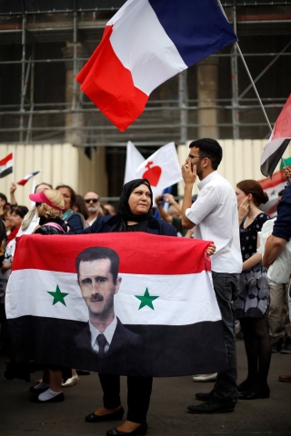 A woman holds a Syrian flag bearing the portrait Bashar al-Assad during a demonstration called by fundamentalist Catholic organisation Civitas in support of Christians of the Middle East on 20 June 2015 in Paris (AFP)