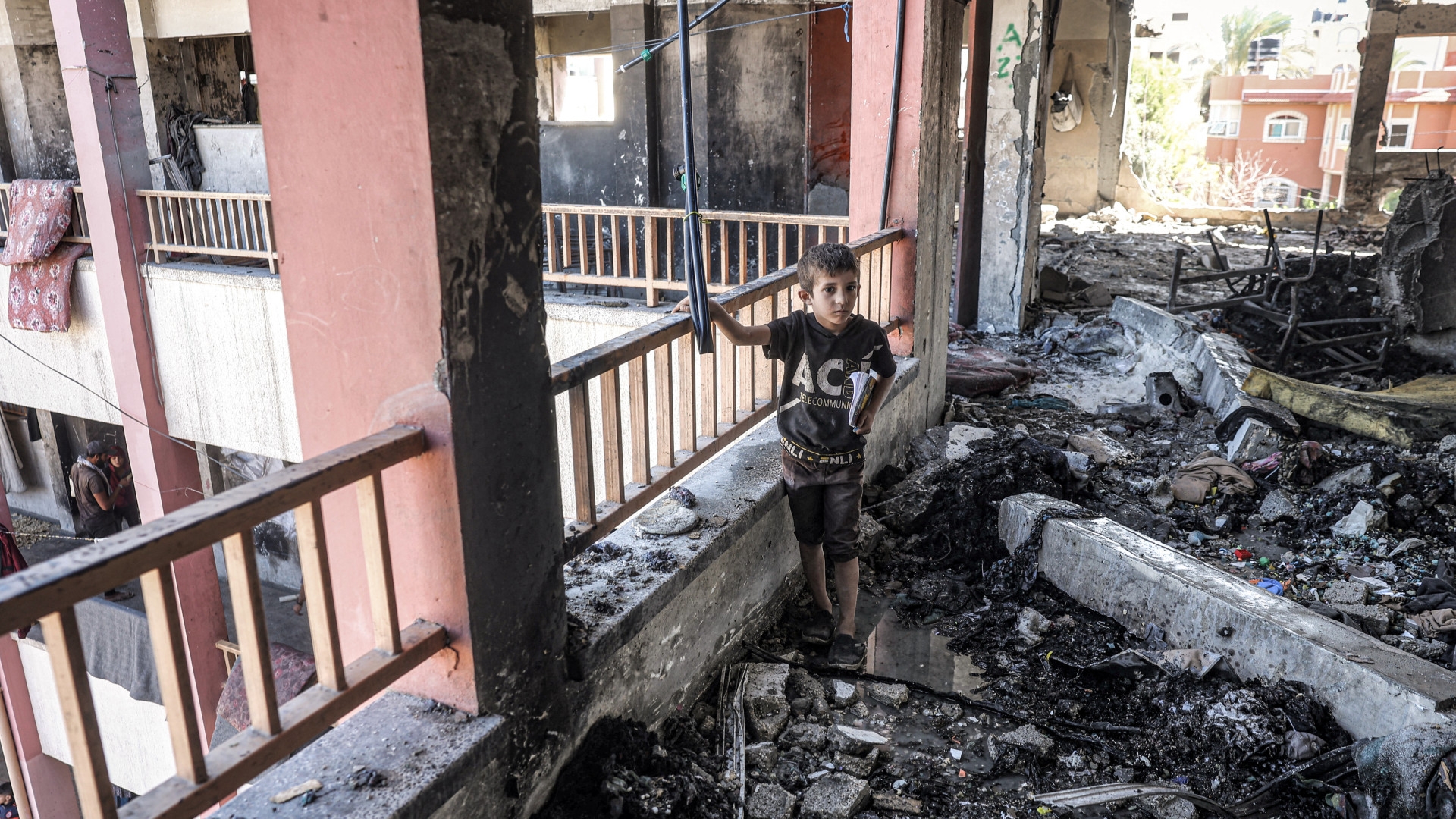 A boy walks with a notebook through debris and rubble in the balcony corridor of the Shuhada school, which was hit by Israeli bombardment, in Nuseirat in the central Gaza Strip on 24 October 2024 (Eyad Baba/AFP)