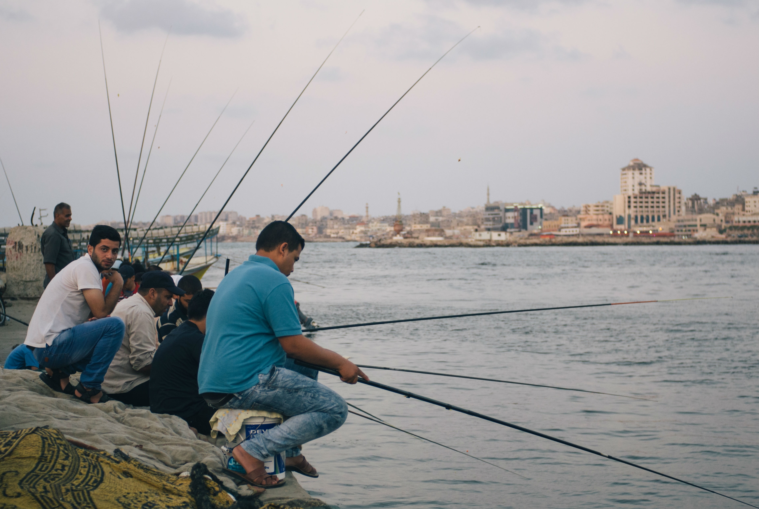 Palestinian men sit together at Gaza's port when they don't have work, which is often for the enclave's many unemployed, drinking coffee as they watch their rods