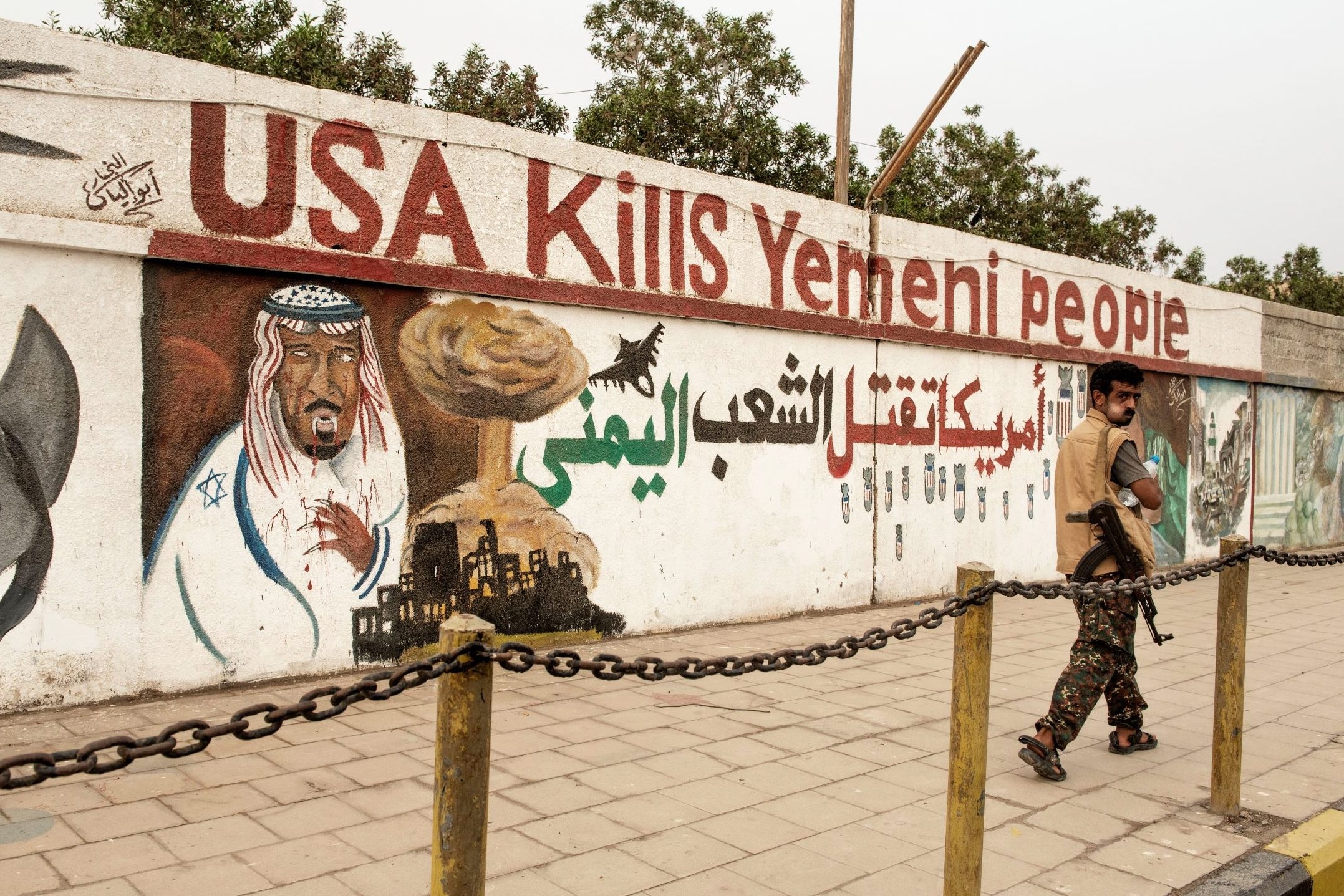 Armed man walks past graffiti saying 'USA Kills Yemeni People' (Alessio Romenzi)
