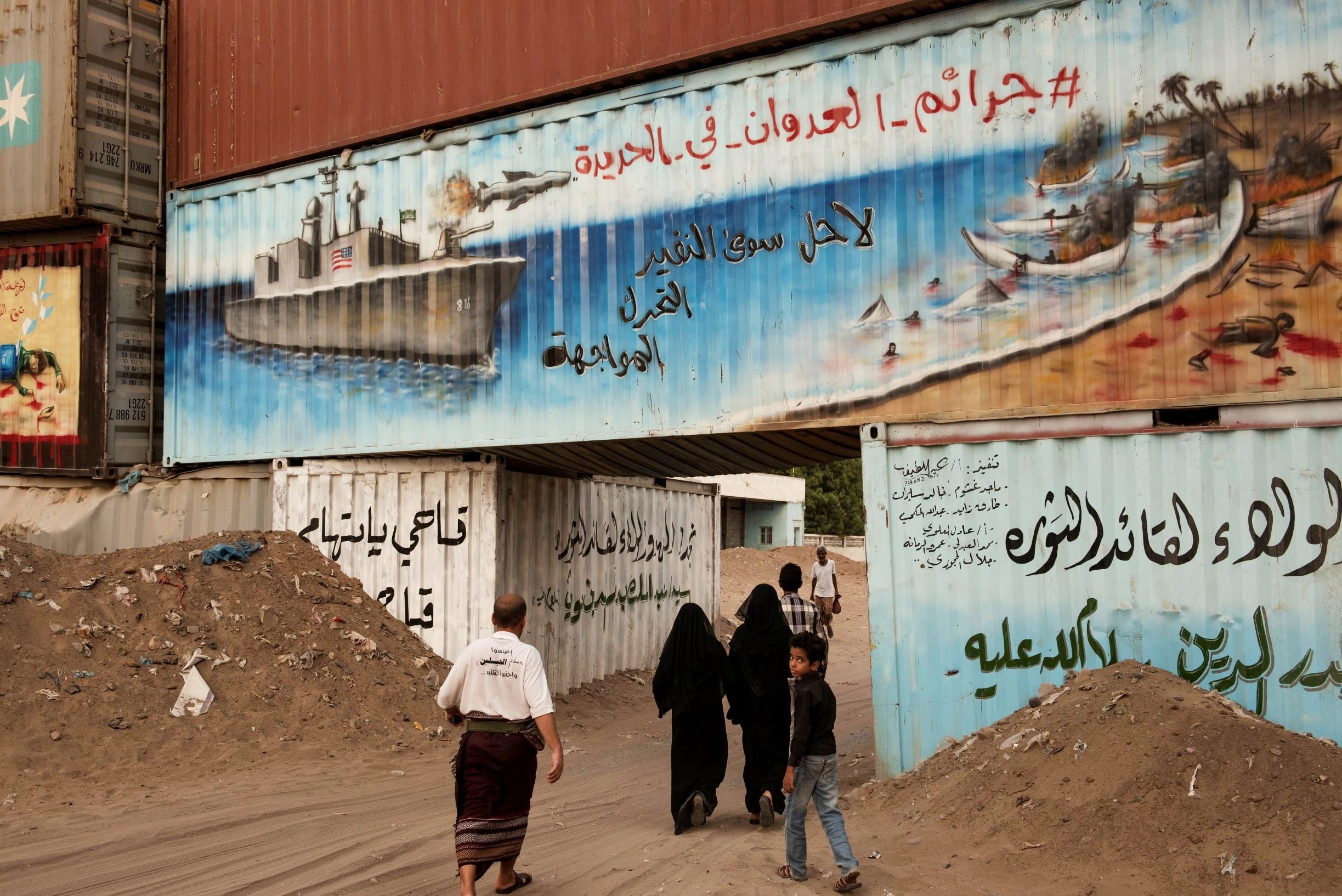 People walk past graffiti with US ship in Hodeidah, Yemen (Alessio Romenzi)