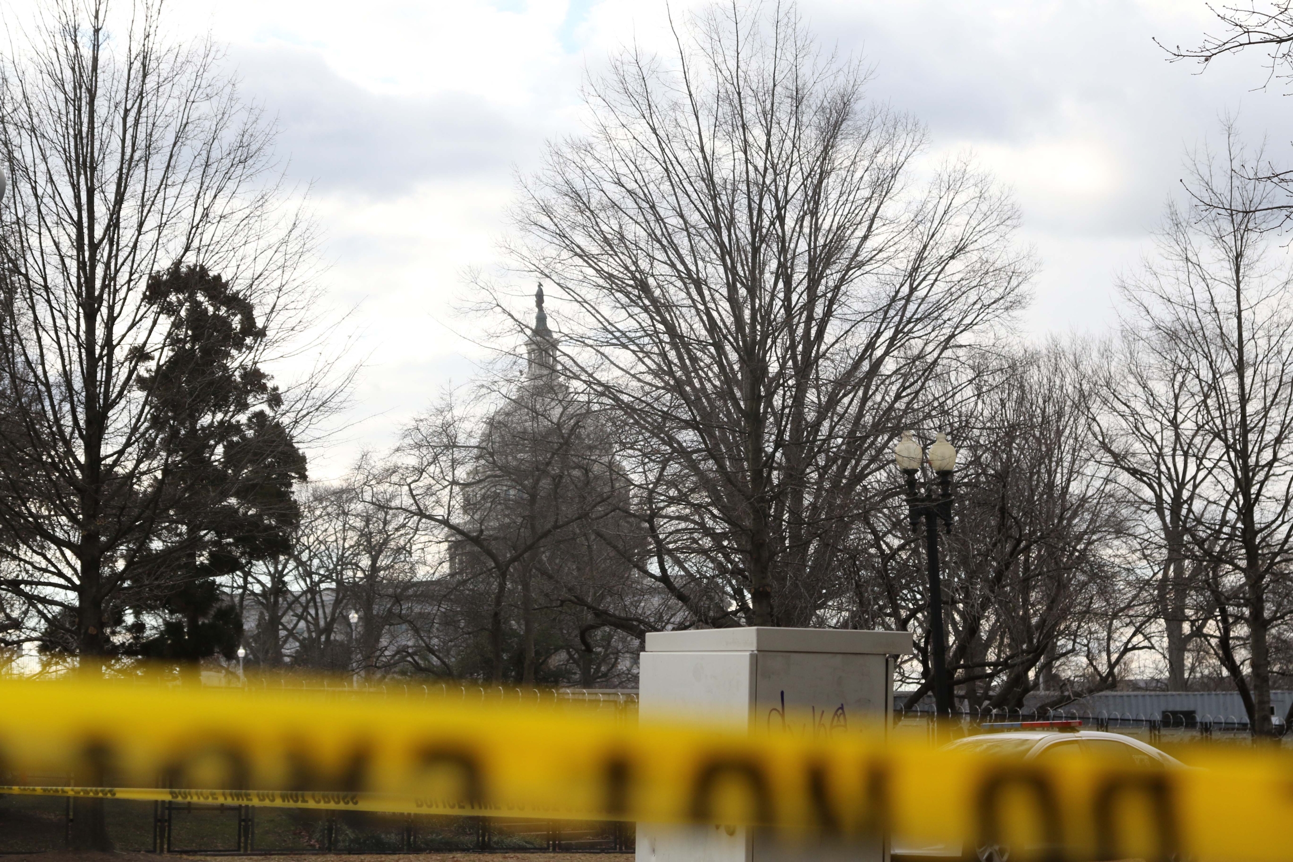 The top of the US Capitol building seen from behind fencing and caution tape.