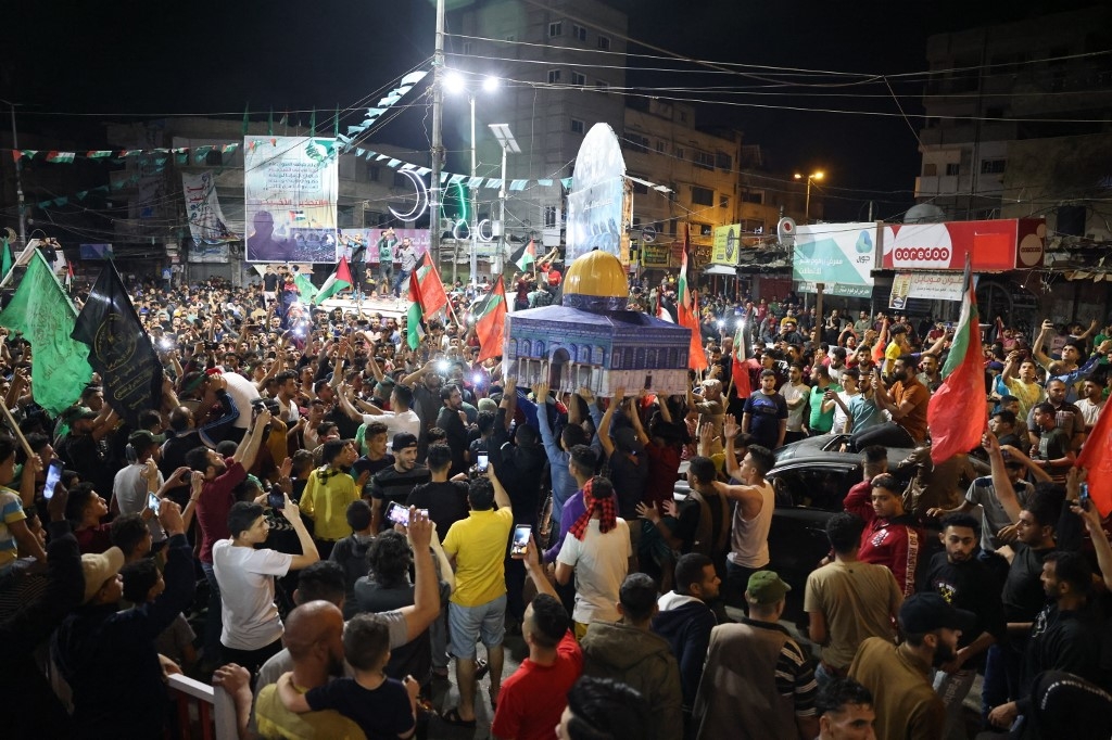 Crowds of Palestinians gather in the streets, waving Palestinian flags, to celebrate in the streets of Khan Yunis. A group of people carry a replica of the Dome of the Rock.