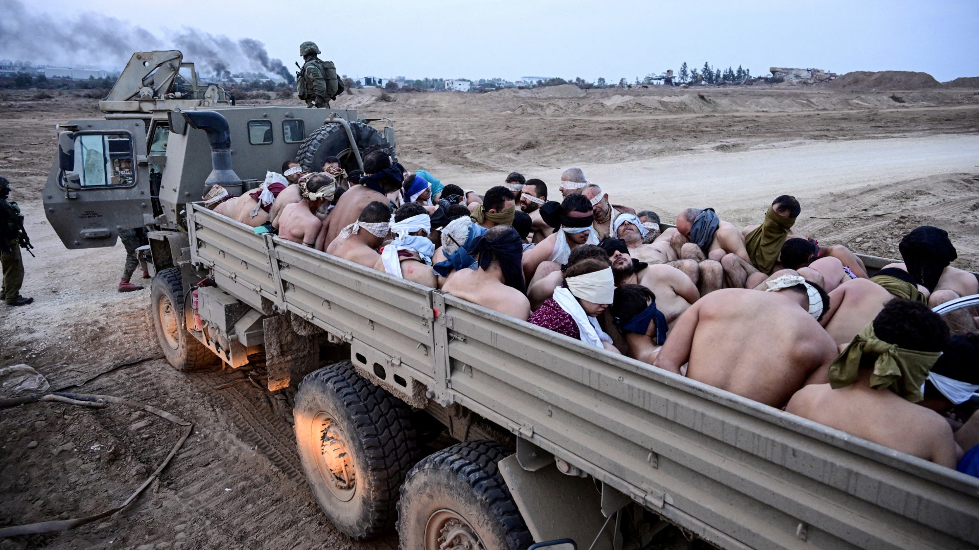 Israeli soldiers stand by a truck packed with shirtless Palestinian detainees in the Gaza Strip on 8 December 2023 (Yossi Zeliger/Reuters)