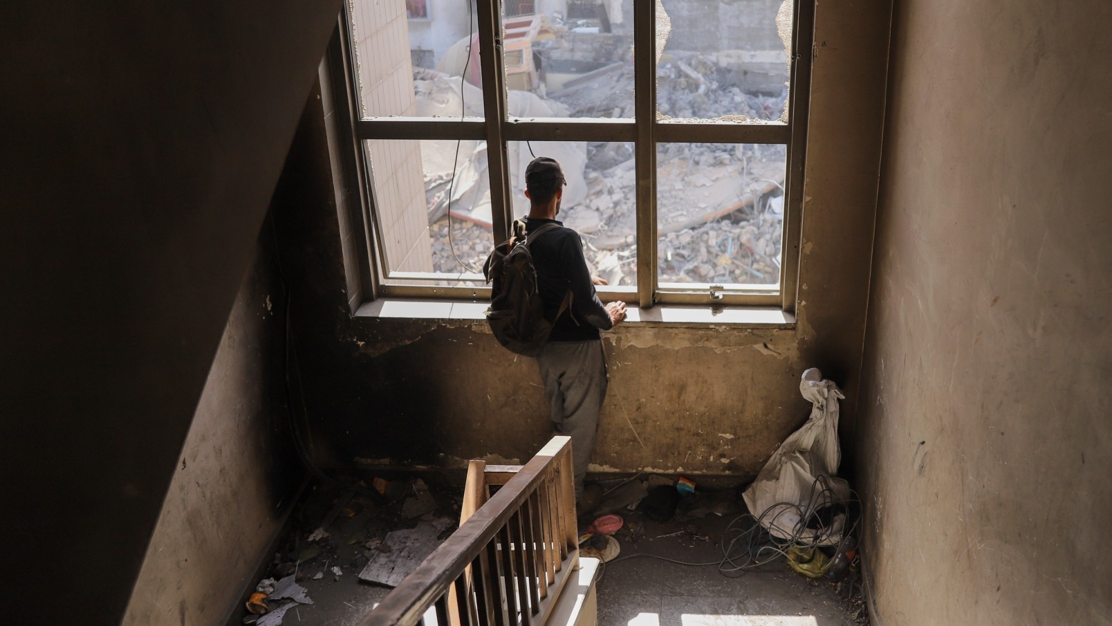 A Palestinian man looks at the devastation in his neighbourhood through a broken set of windows following Israeli air strikes on Gaza City (MEE/Mohammed al-Hajjar)