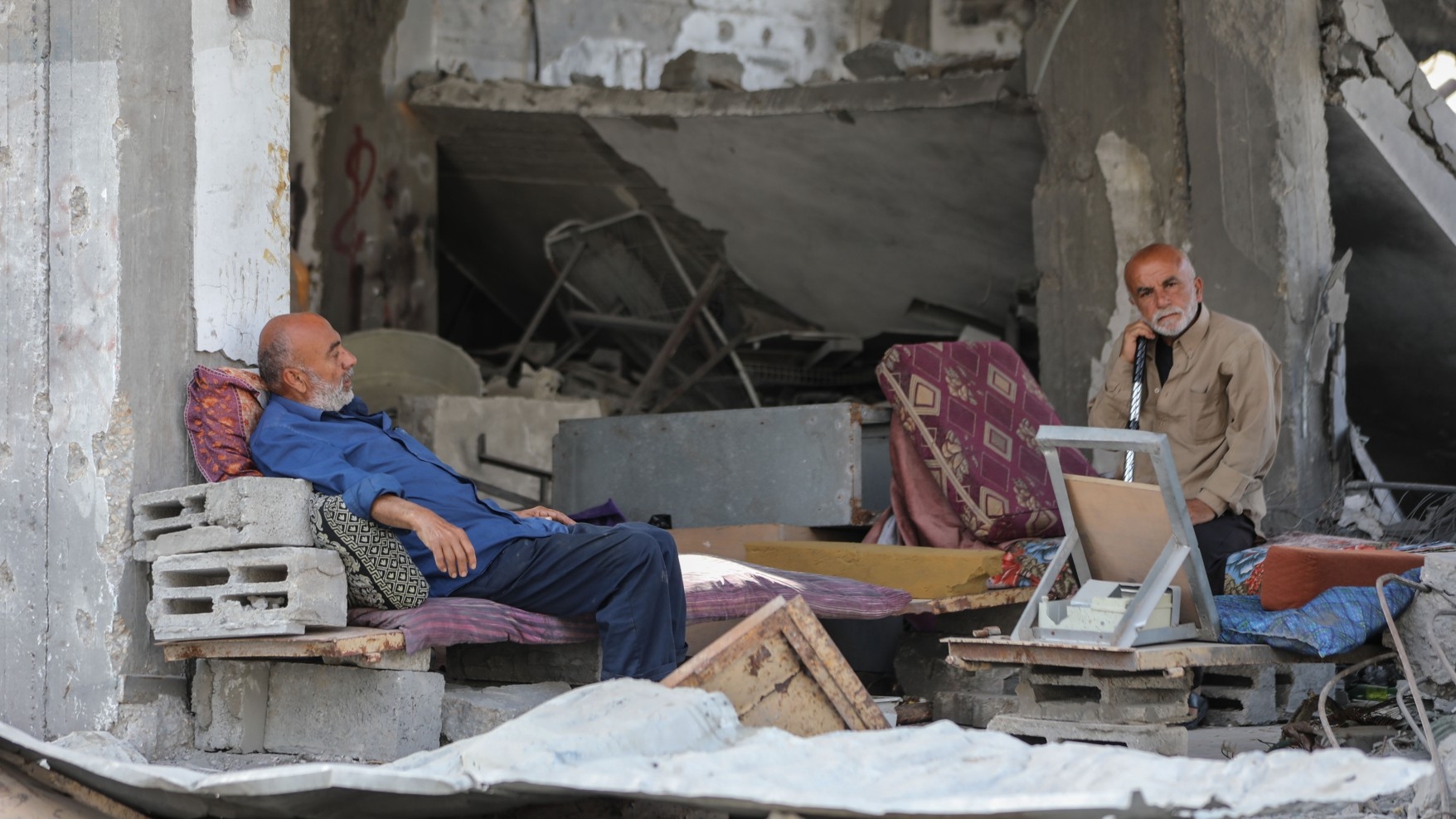 Two Palestinian men sit amid the rubble of their home in Gaza City that was targeted by Israeli fighter jets (MEE/Mohammed al-Hajjar)