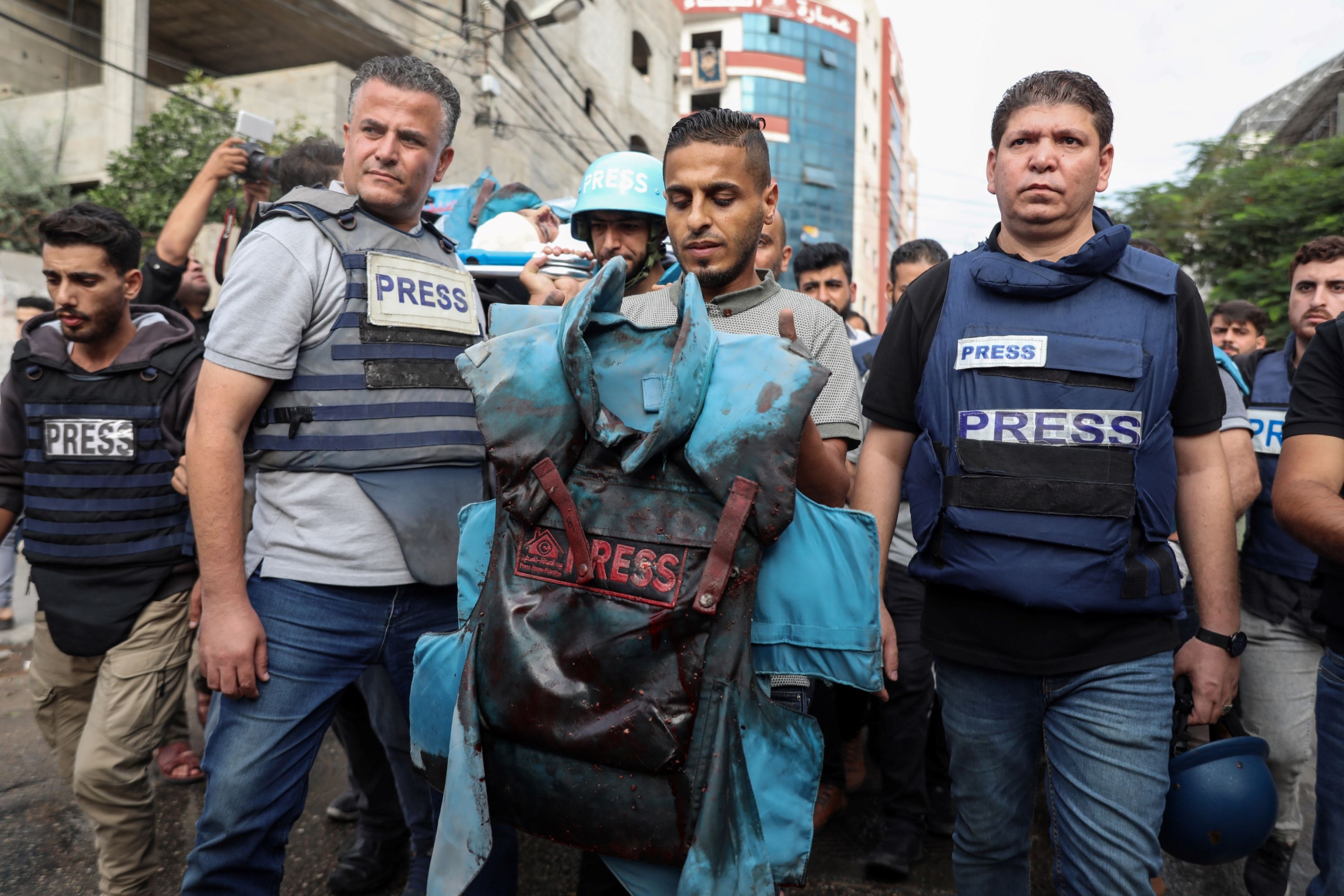 The colleagues of three slain Palestinian journalists raise a blood soaked press jacket at their funeral in Gaza City on 10 October, 2023 (MEE/Mohammed al-Hajjar)