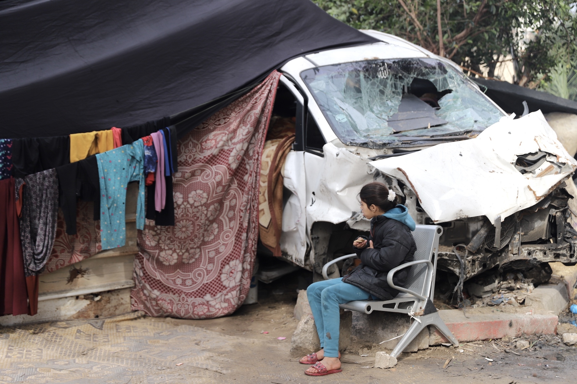 A girl can be seen near a bombed-out car which has been turned into a makeshift shelter in Gaza City on 21 January, 2024 (MEE/Mohammed al-Hajjar)