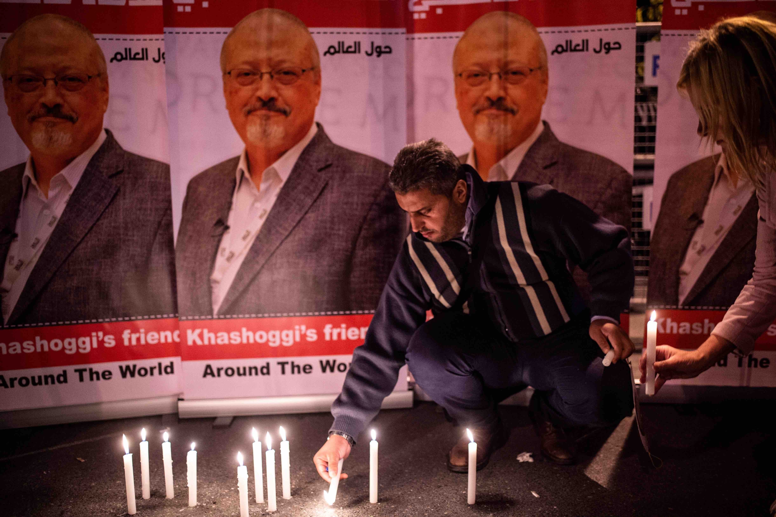 A man lights a candle by posters of slain Saudi journalist Jamal Khashoggi during a gathering outside the Saudi Arabian consulate in Istanbul on 2 October 2018 (AFP)